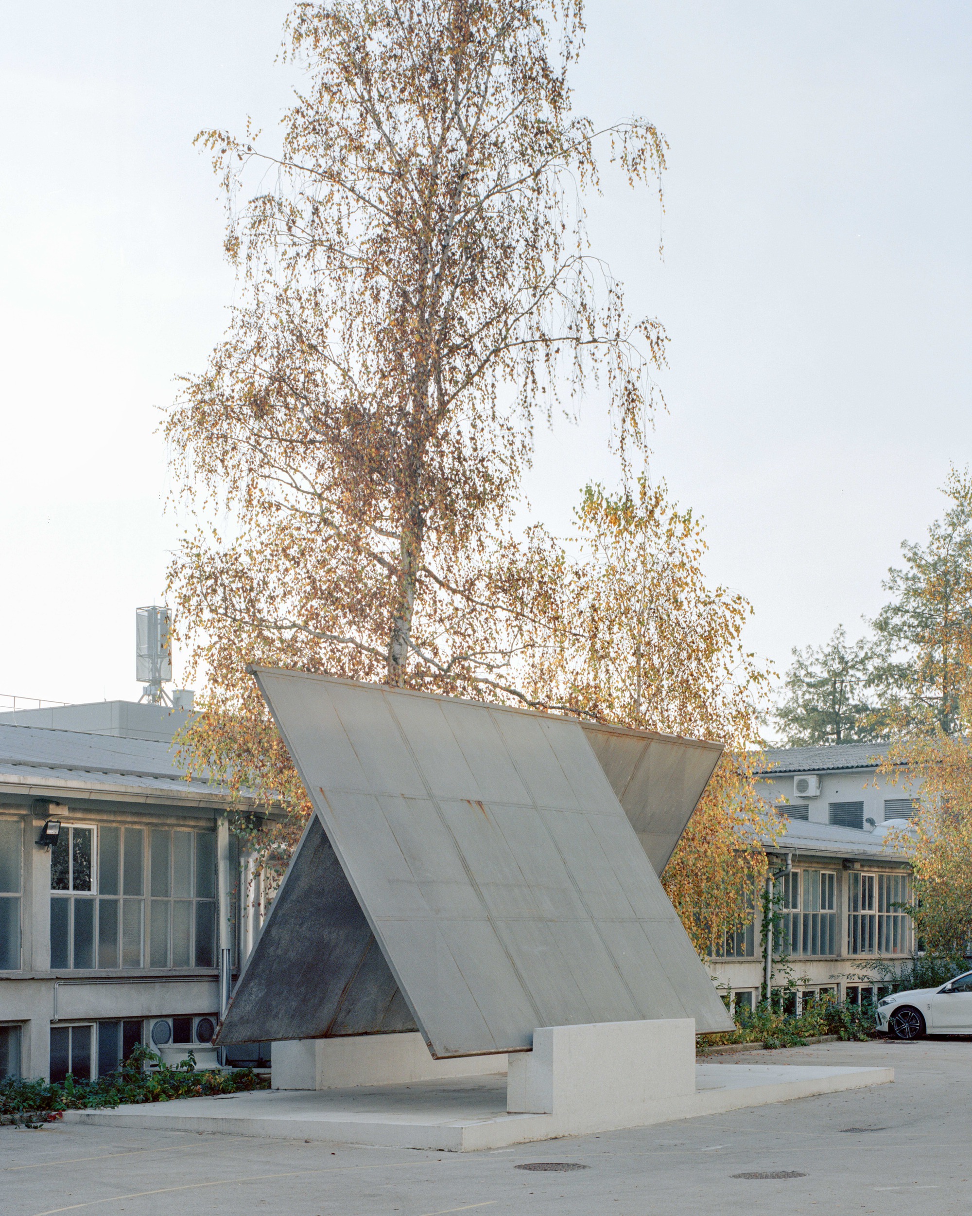 Folded concrete canopy structure supported on two vertical piers with autumn birch tree behind
