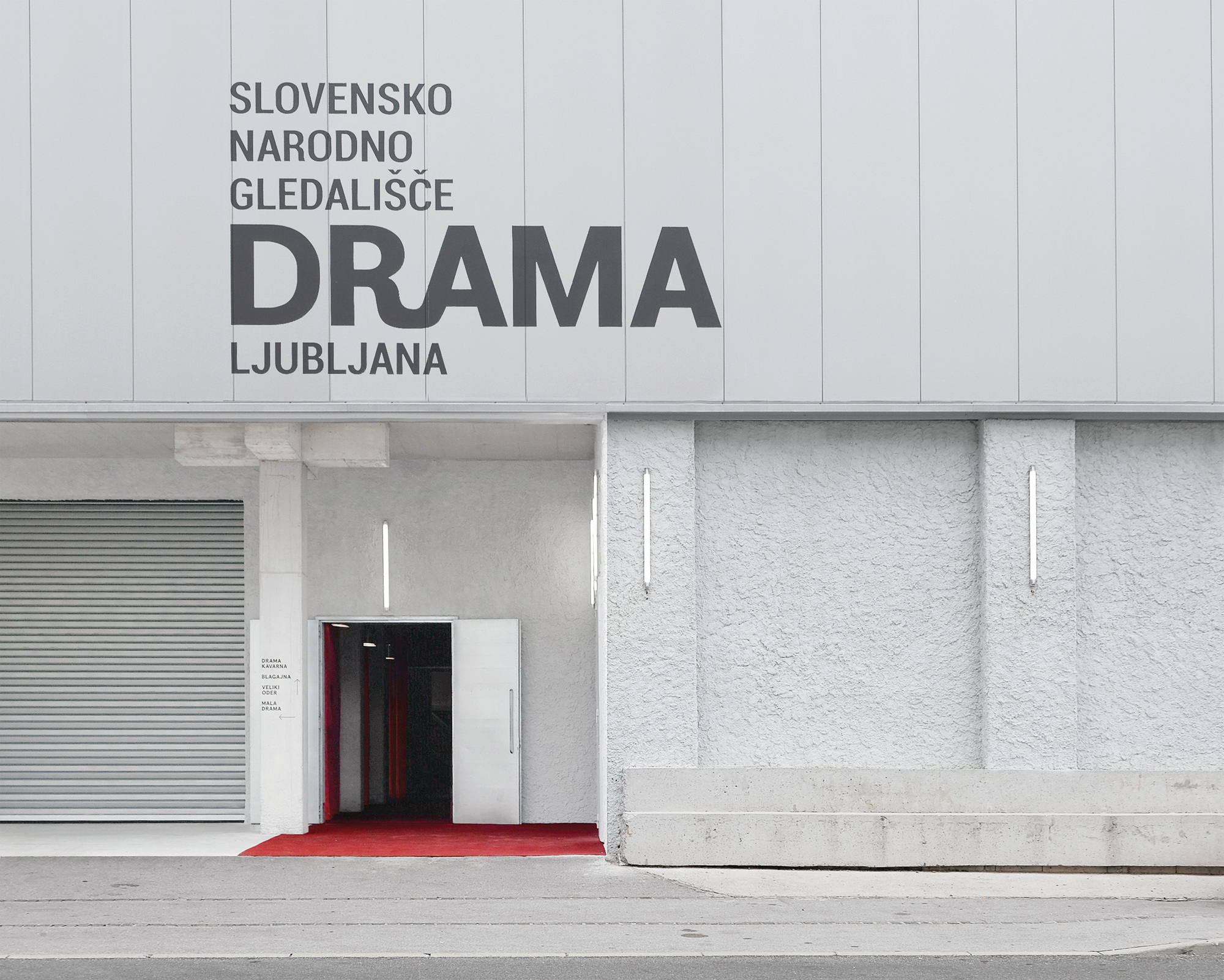 Entrance facade with textured white plaster panels, red carpet threshold, and graphic lettering above