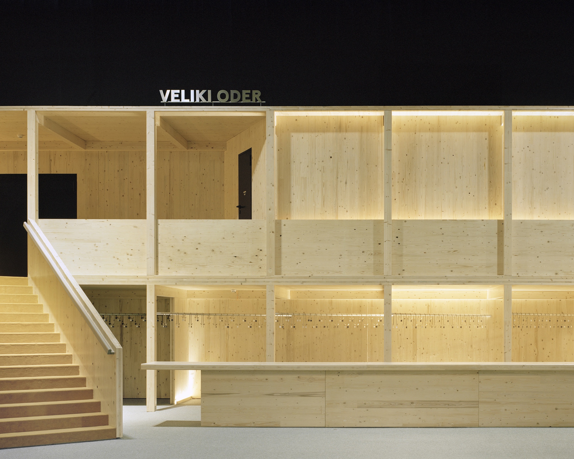Interior view of laminated timber wall framing and staircase under warm artificial light at night