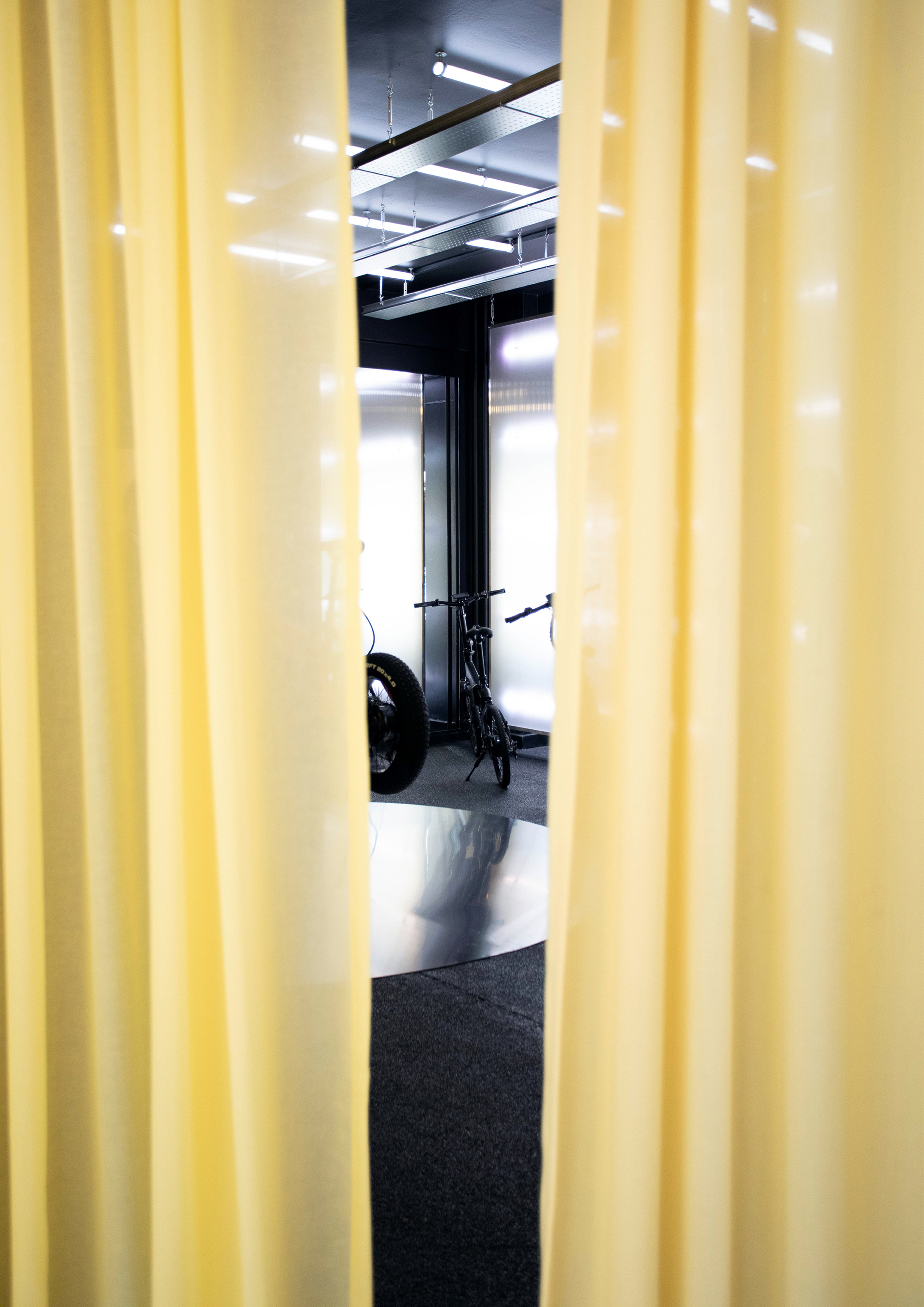 View through yellow pleated curtains into showroom space with exposed ceiling and black floor