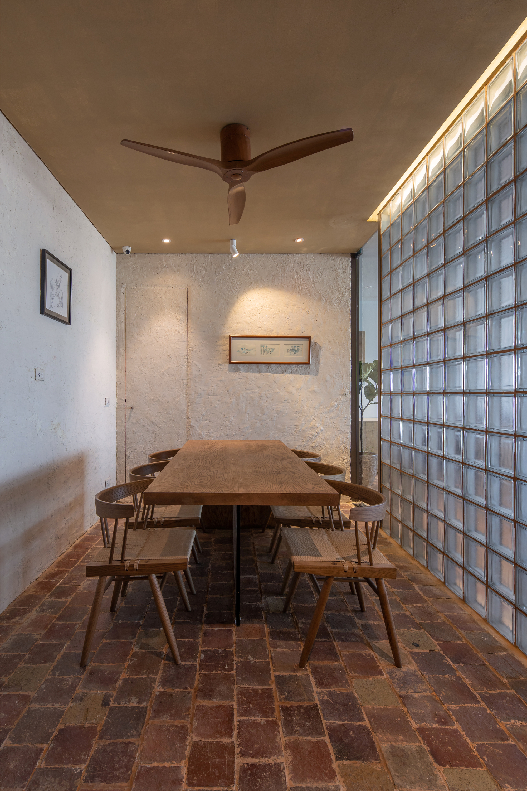 Dining area with timber table and chairs on reclaimed brick floor beneath timber ceiling fan and pendant light