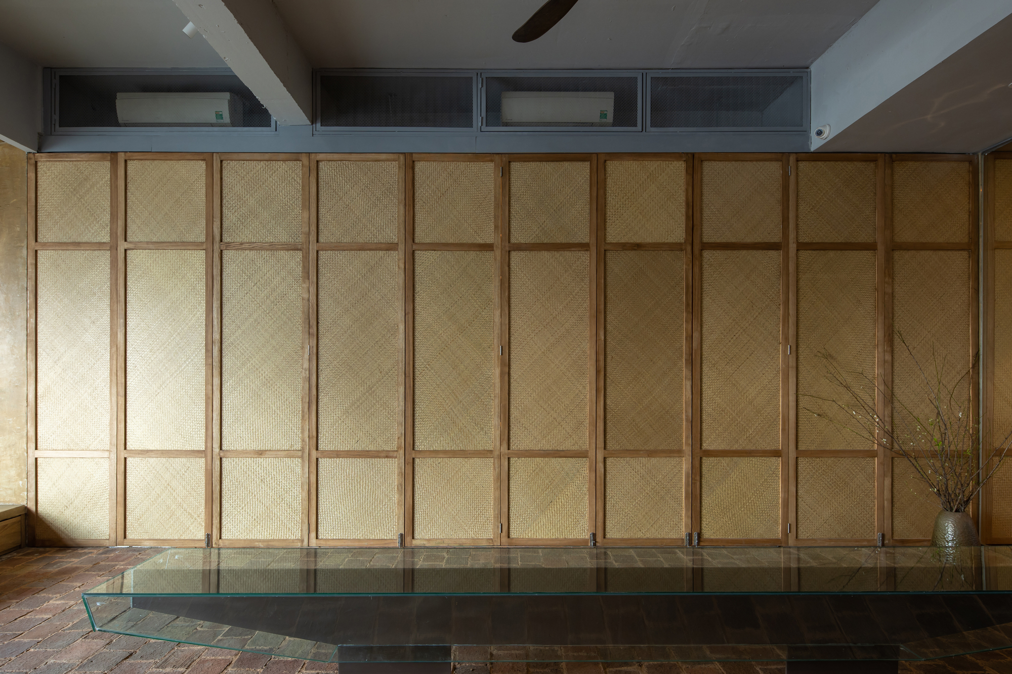 Closed woven timber partition wall with raised platform and terracotta brick floor at base