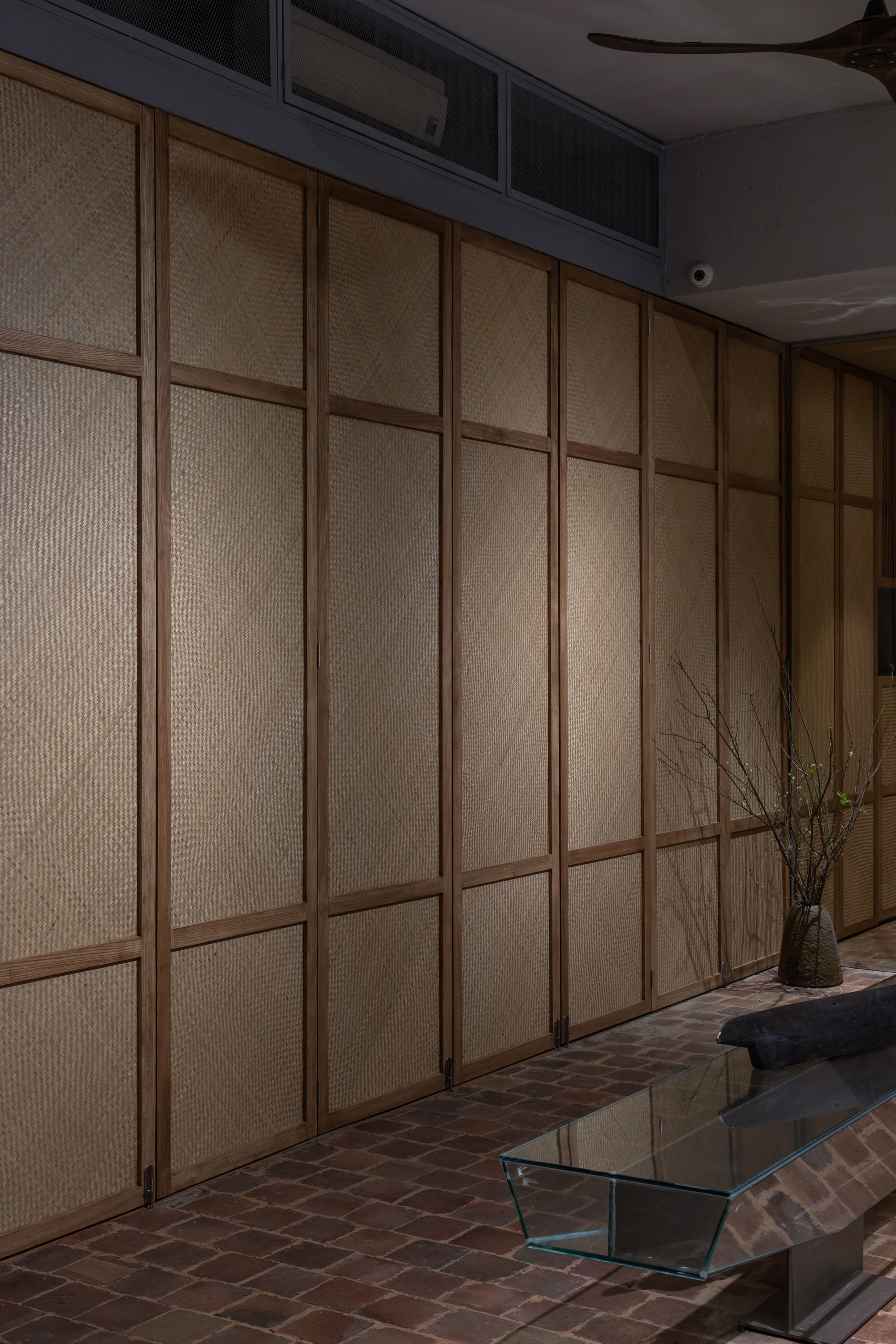 Textured rattan panel wall with timber framing adjacent to brick floor and glass coffee table