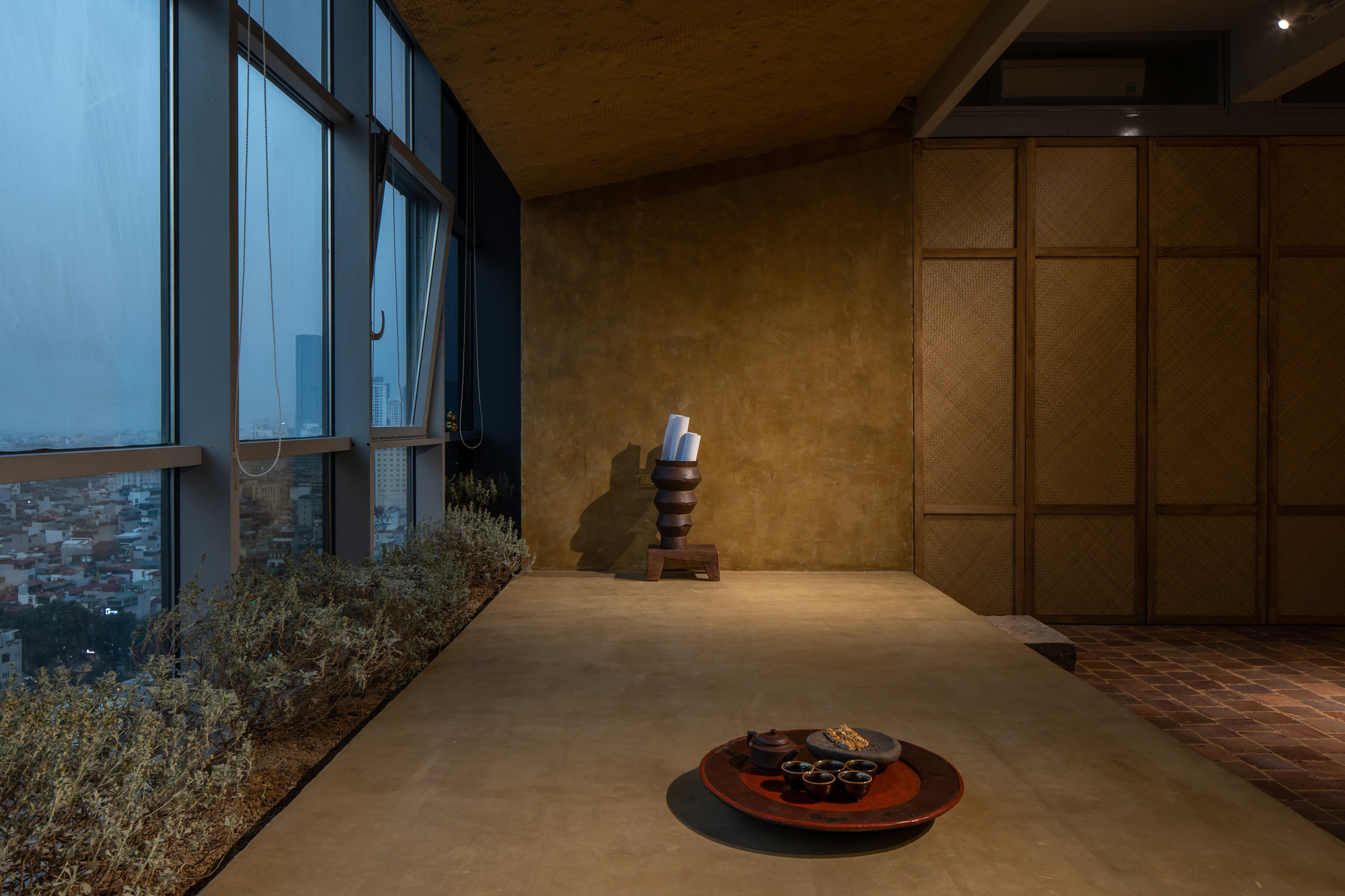 Window bay with planted bed and sculpture beside woven storage wall at dusk