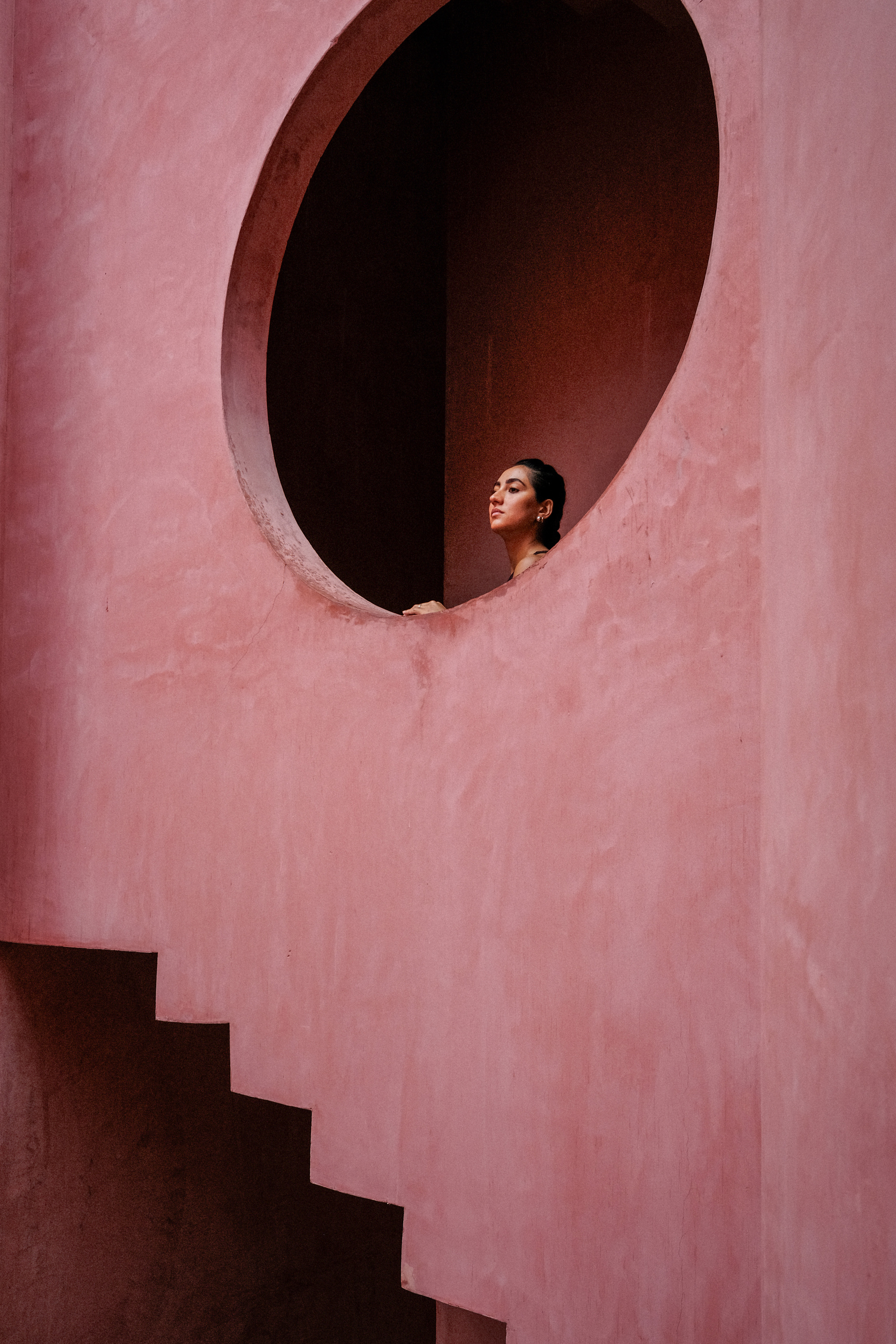 Oval opening in a pink plastered wall with a figure looking out and a staircase below