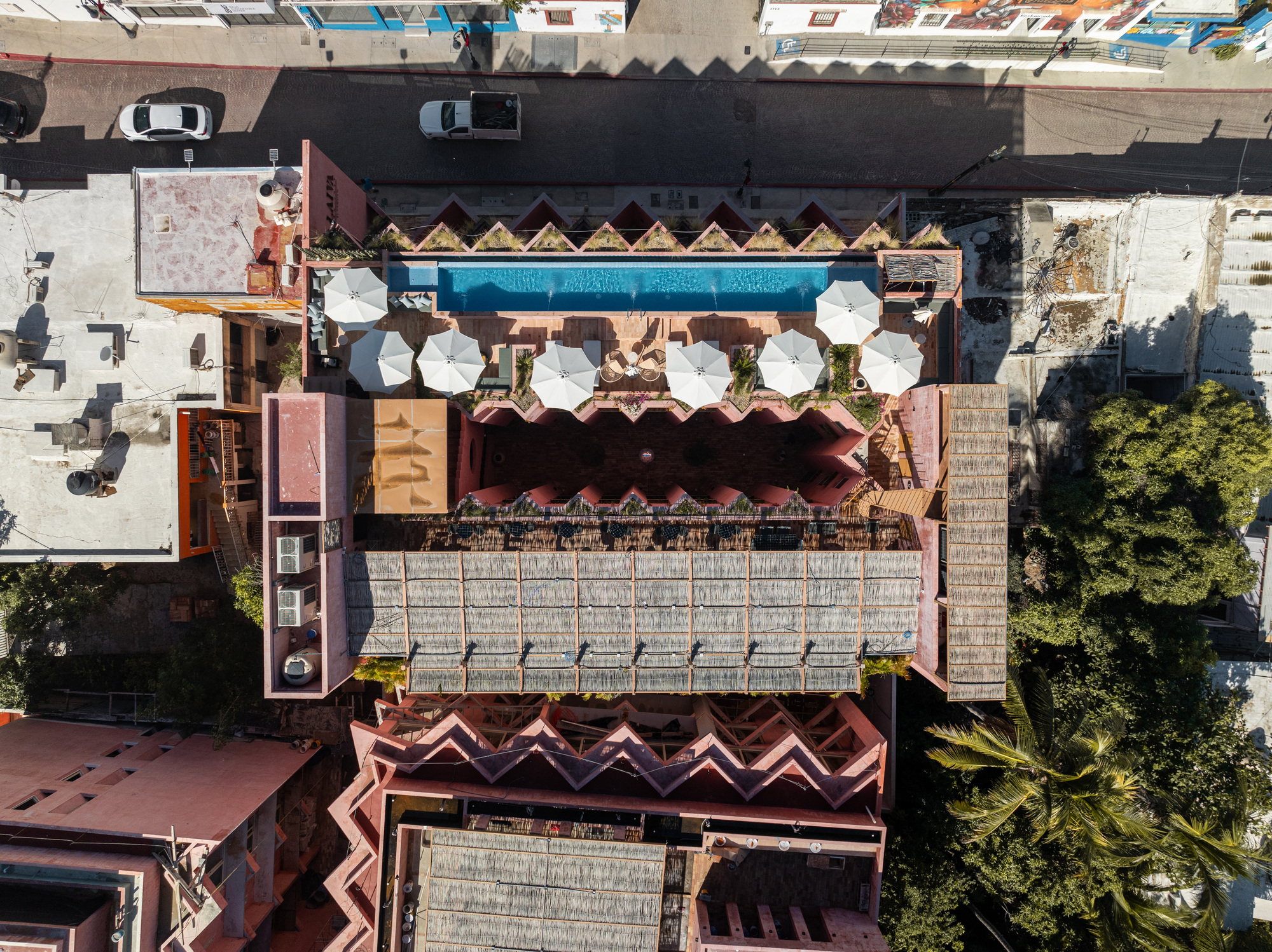 Drone view showing the sawtooth roof, white umbrellas on the terrace and adjacent street with parked cars