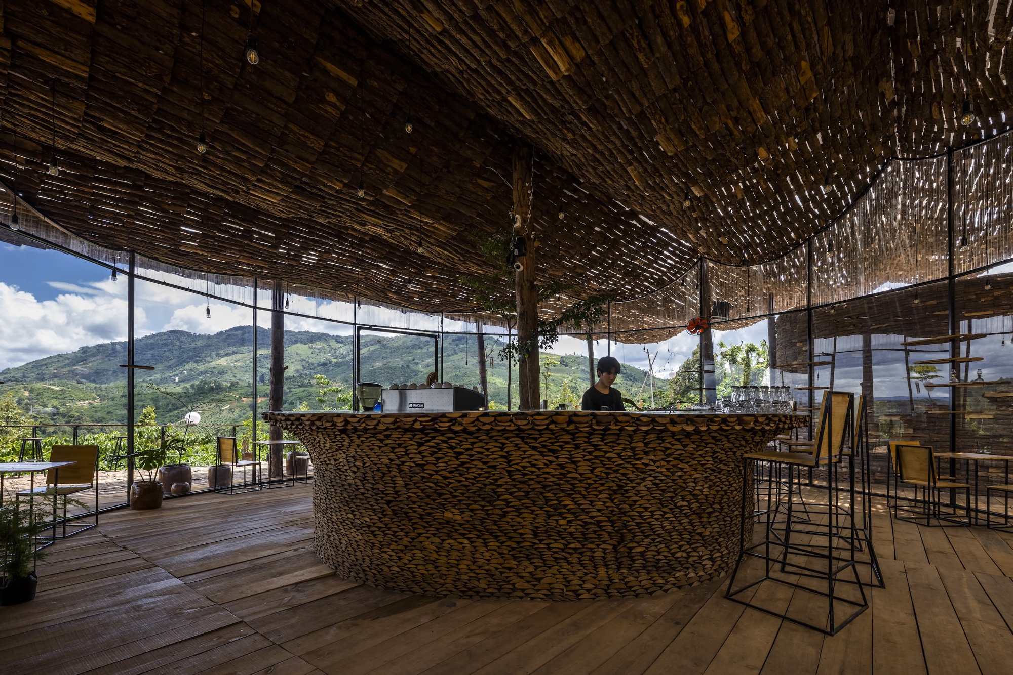 Interior bar counter wrapped in woven material under the bamboo ceiling with mountain vista through glazing