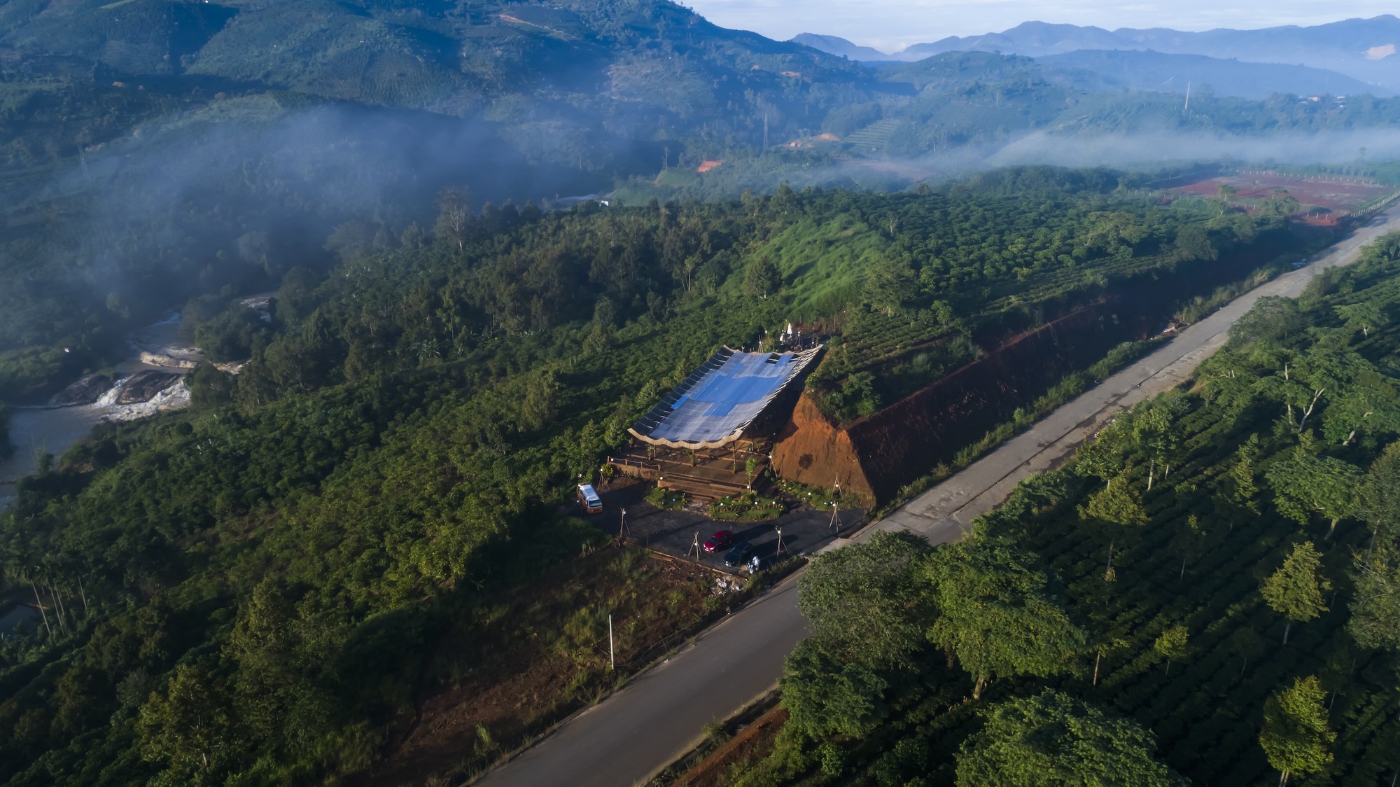 Aerial view of the compound on a forested ridgeline with morning mist in the valley below