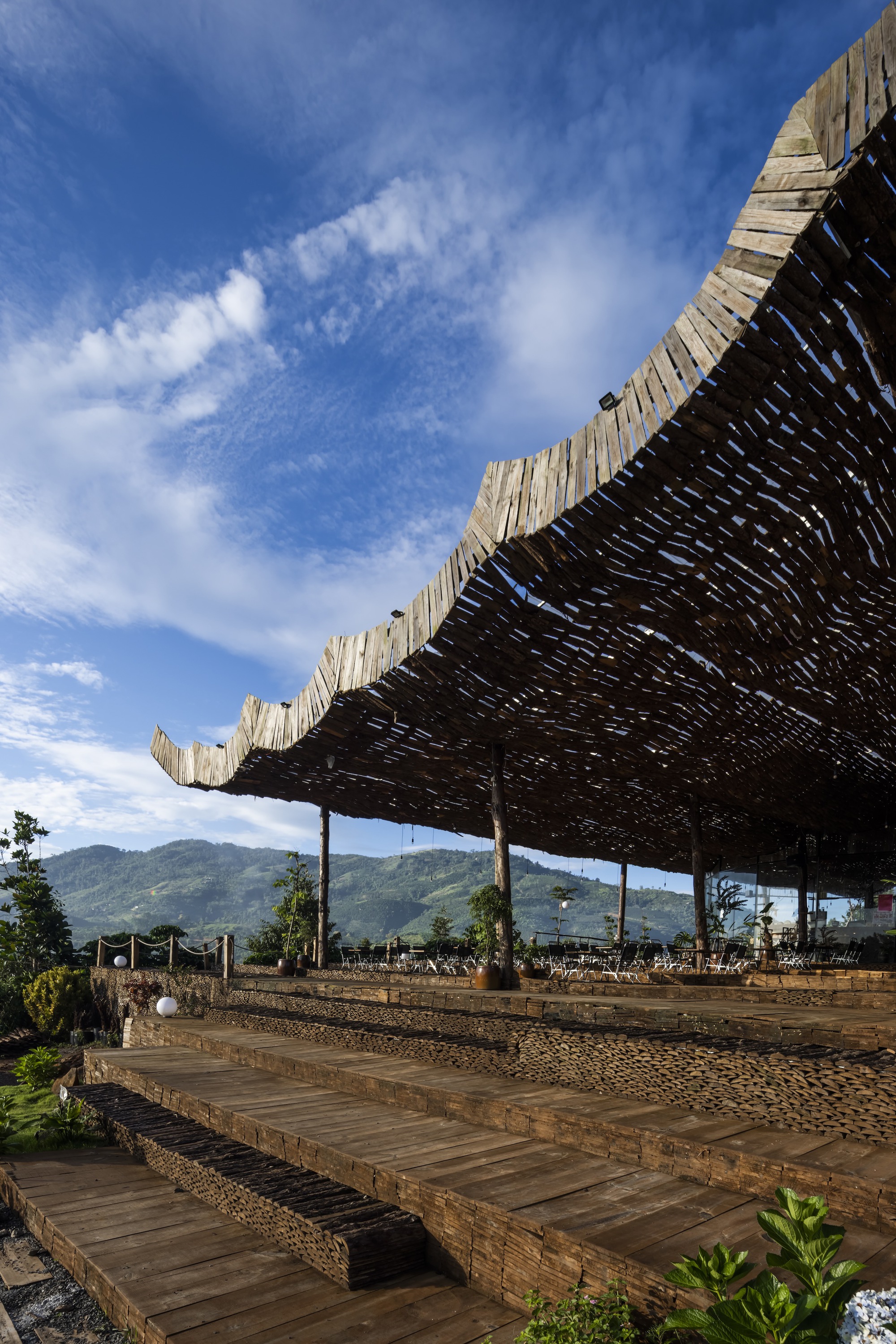 Stepped timber platforms leading up to the woven bamboo roof structure against distant green peaks