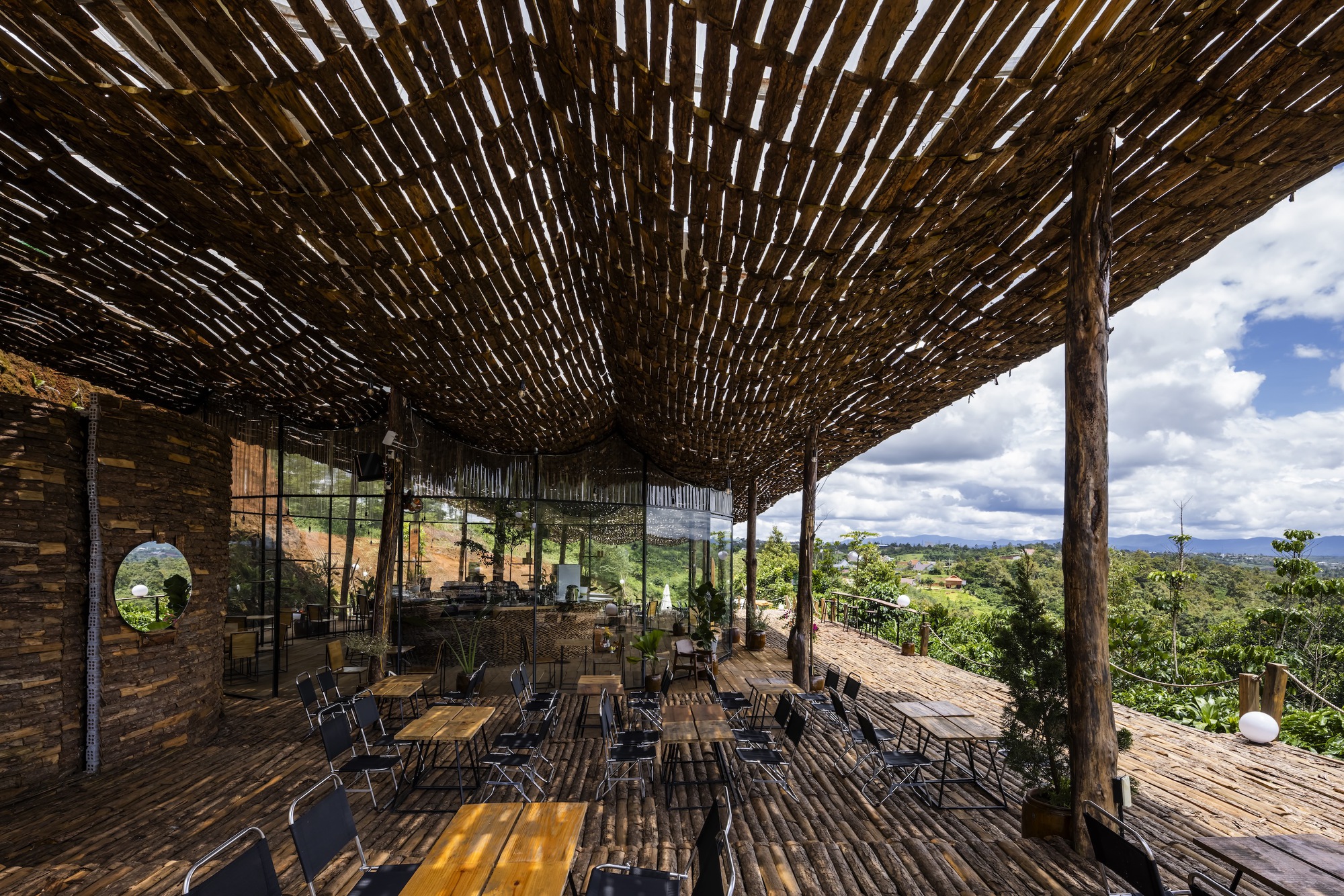 Dining area beneath a curved lattice roof supported by rustic timber posts with views to distant hills