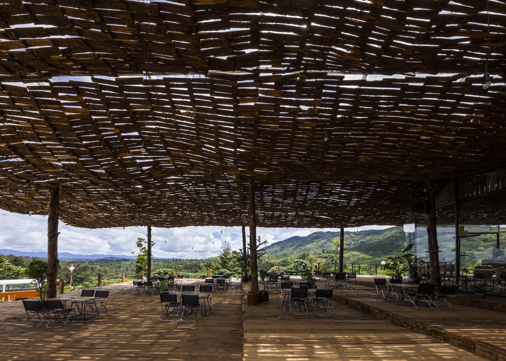 Dappled light filtering through the woven bamboo ceiling onto the timber deck and seating below
