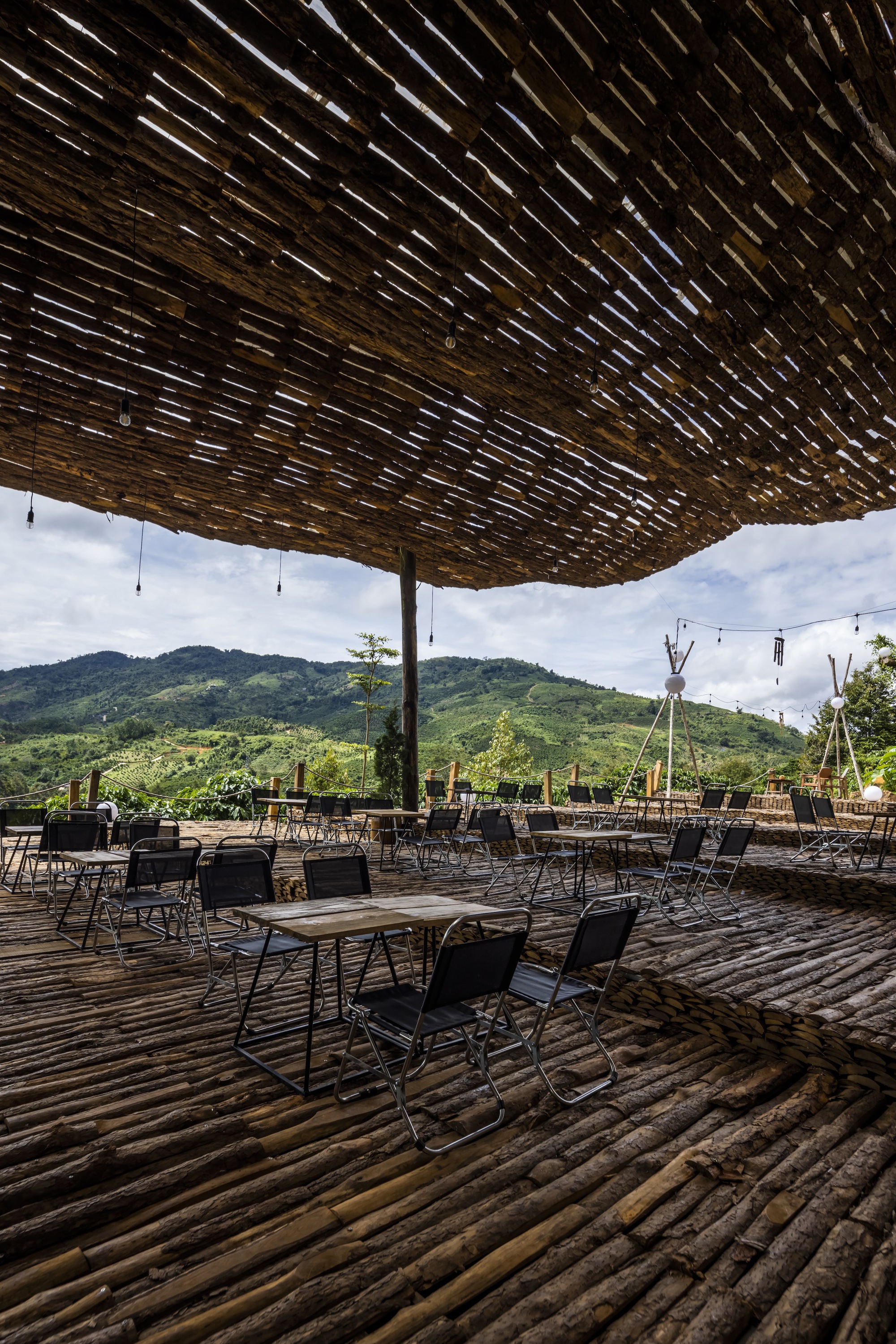 Outdoor dining area beneath woven bamboo canopy on split bamboo flooring with mountain backdrop