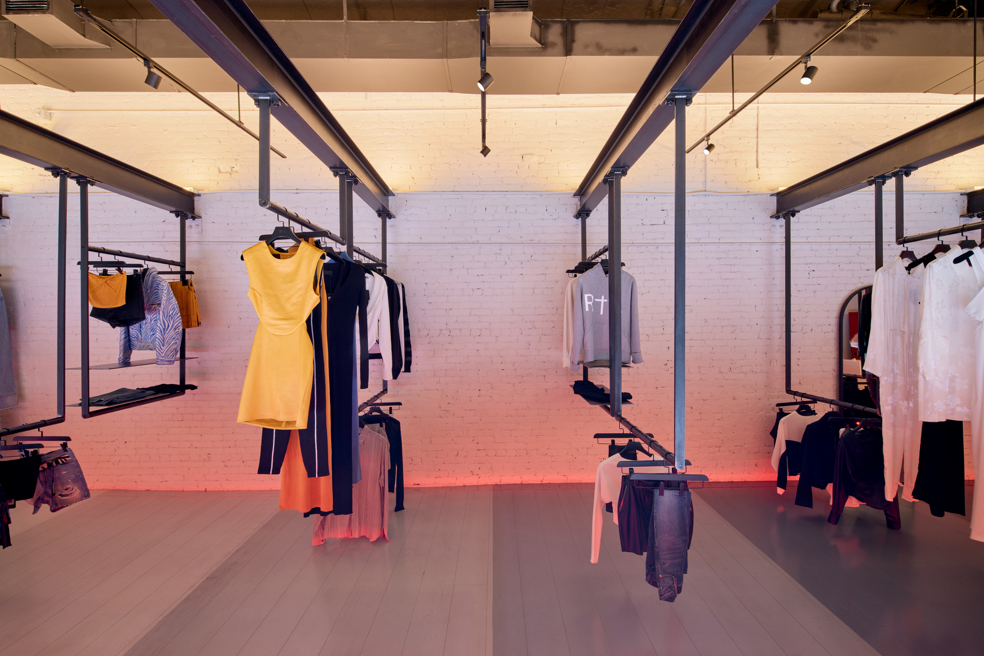 Freestanding clothing racks beneath steel frame supports with painted brick wall bathed in red light