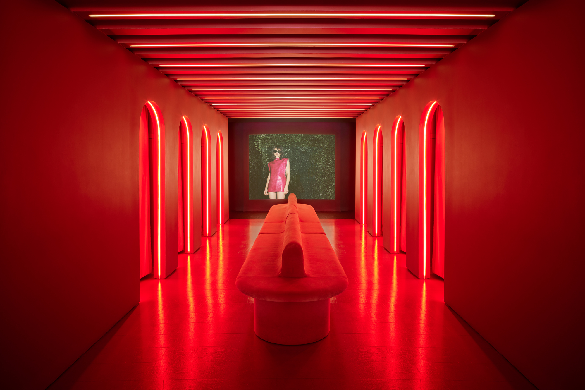 Red neon-lit corridor with arched niches along the walls and a central upholstered bench