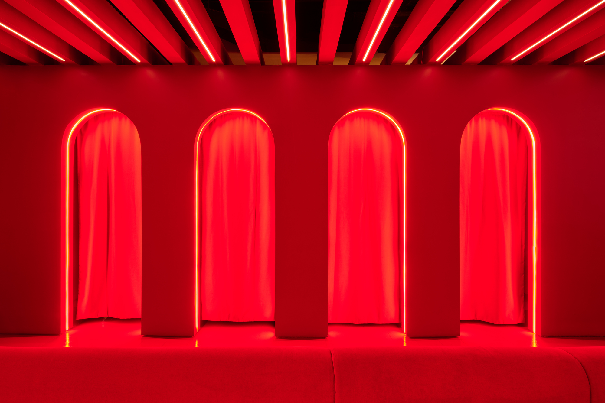 Four arched alcoves with red neon frames and draped curtains along a red-painted wall