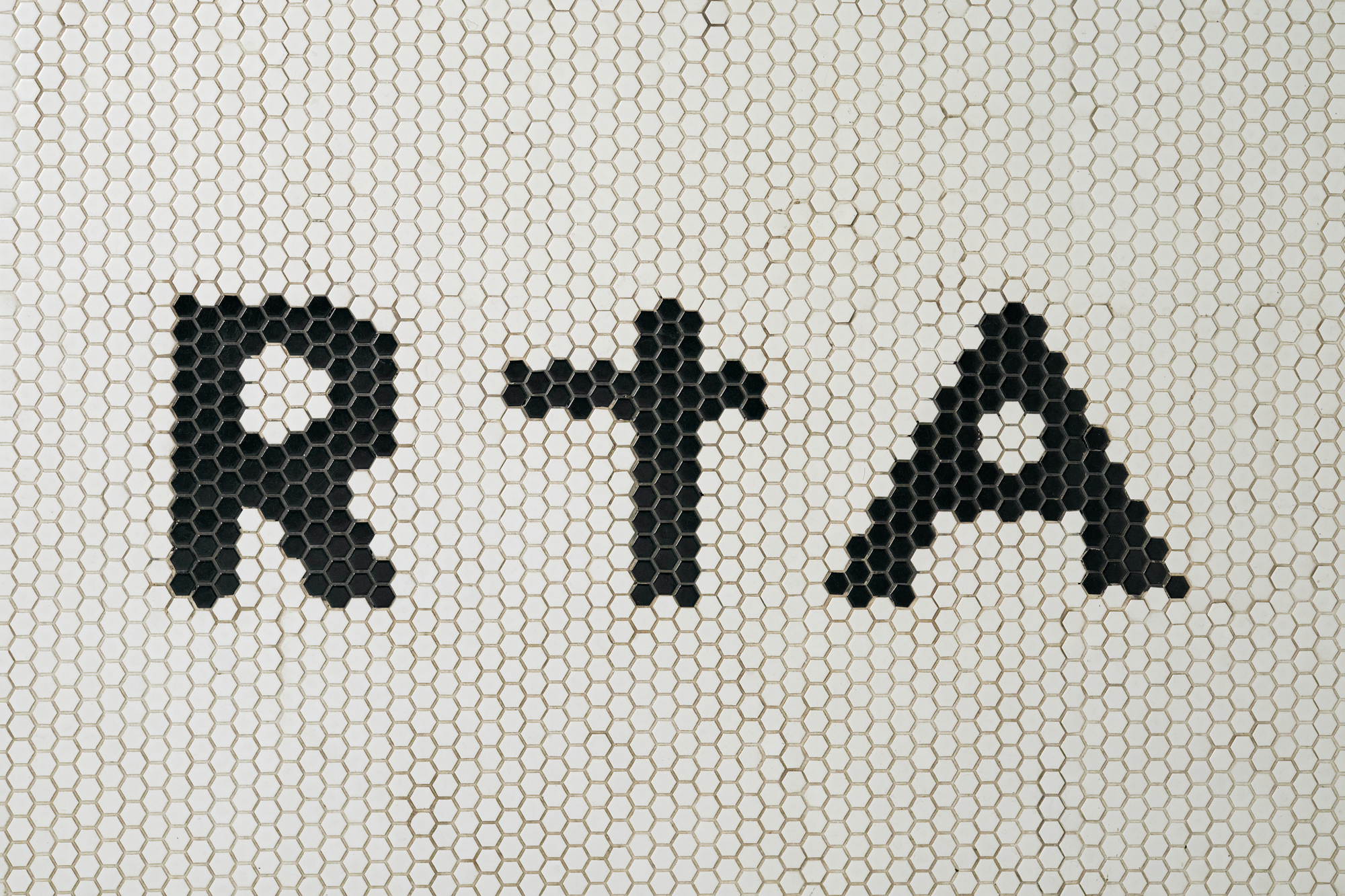 Black hexagonal mosaic tiles spelling letters on a white penny tile wall