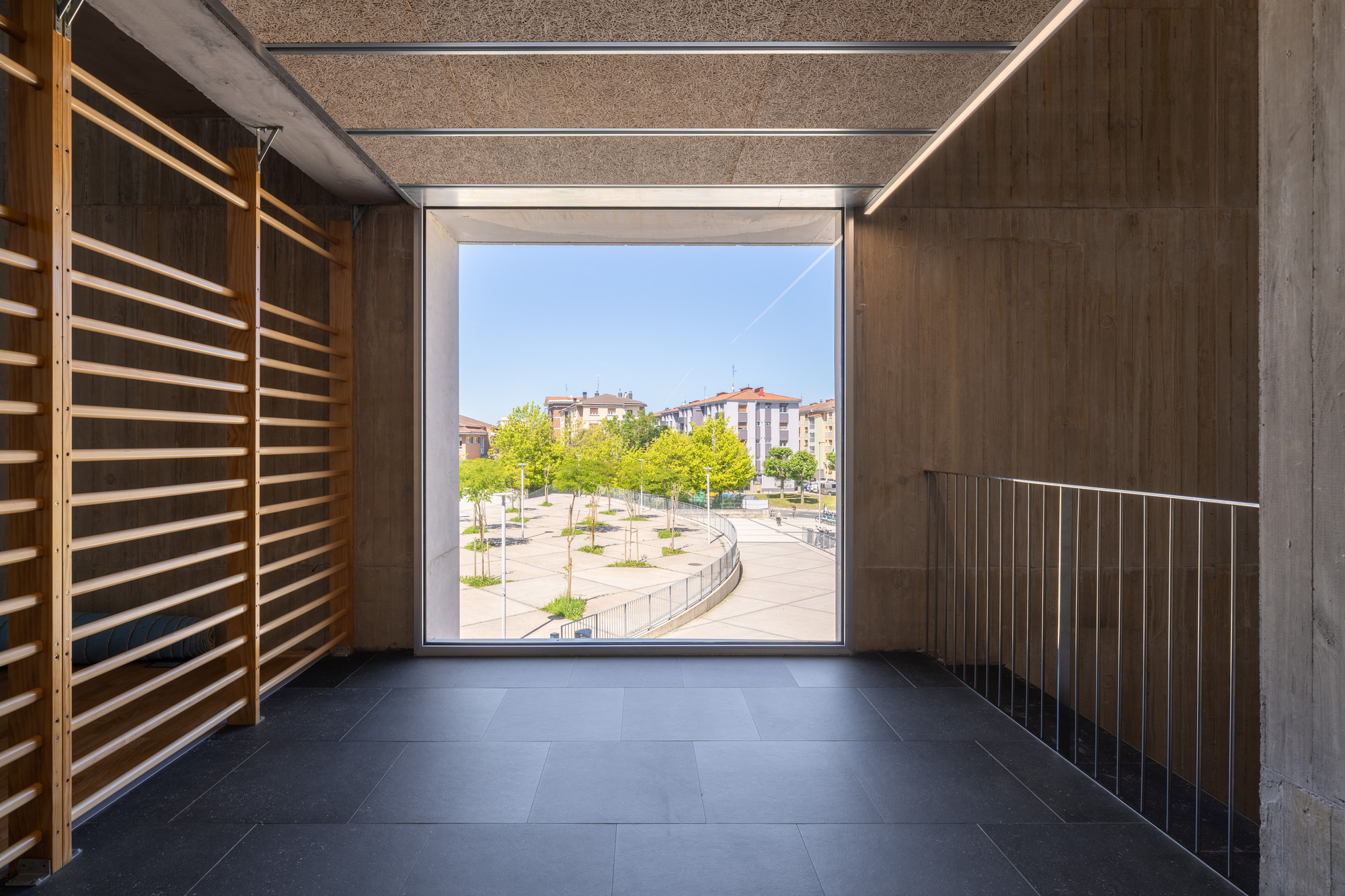 Timber-lined passageway framing a view of the tree-lined plaza through a square opening