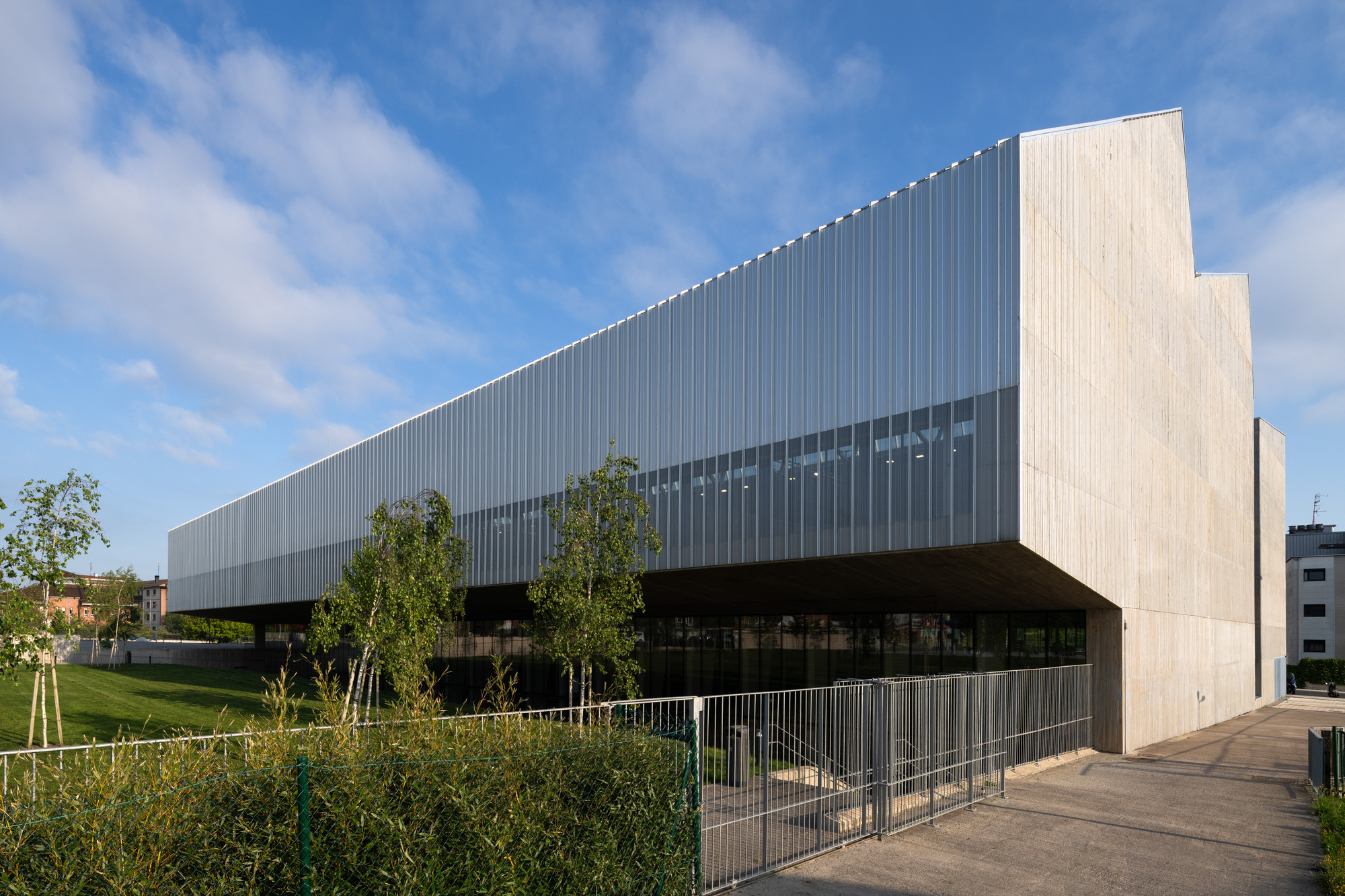 Cantilevered corrugated metal facade with horizontal band of windows above a planted lawn with young trees