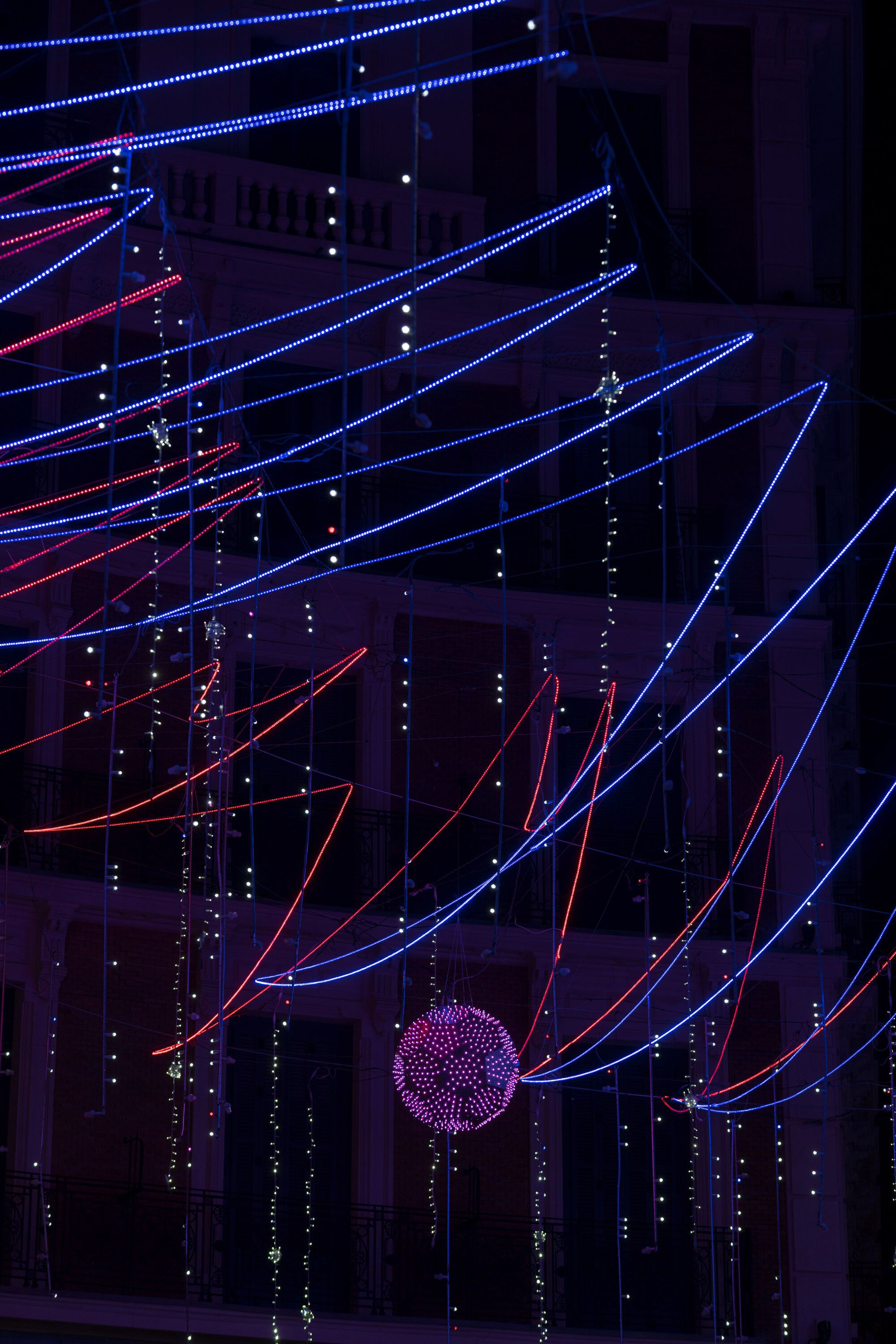 Suspended LED light tubes in red and blue converging toward a spherical purple fixture at night