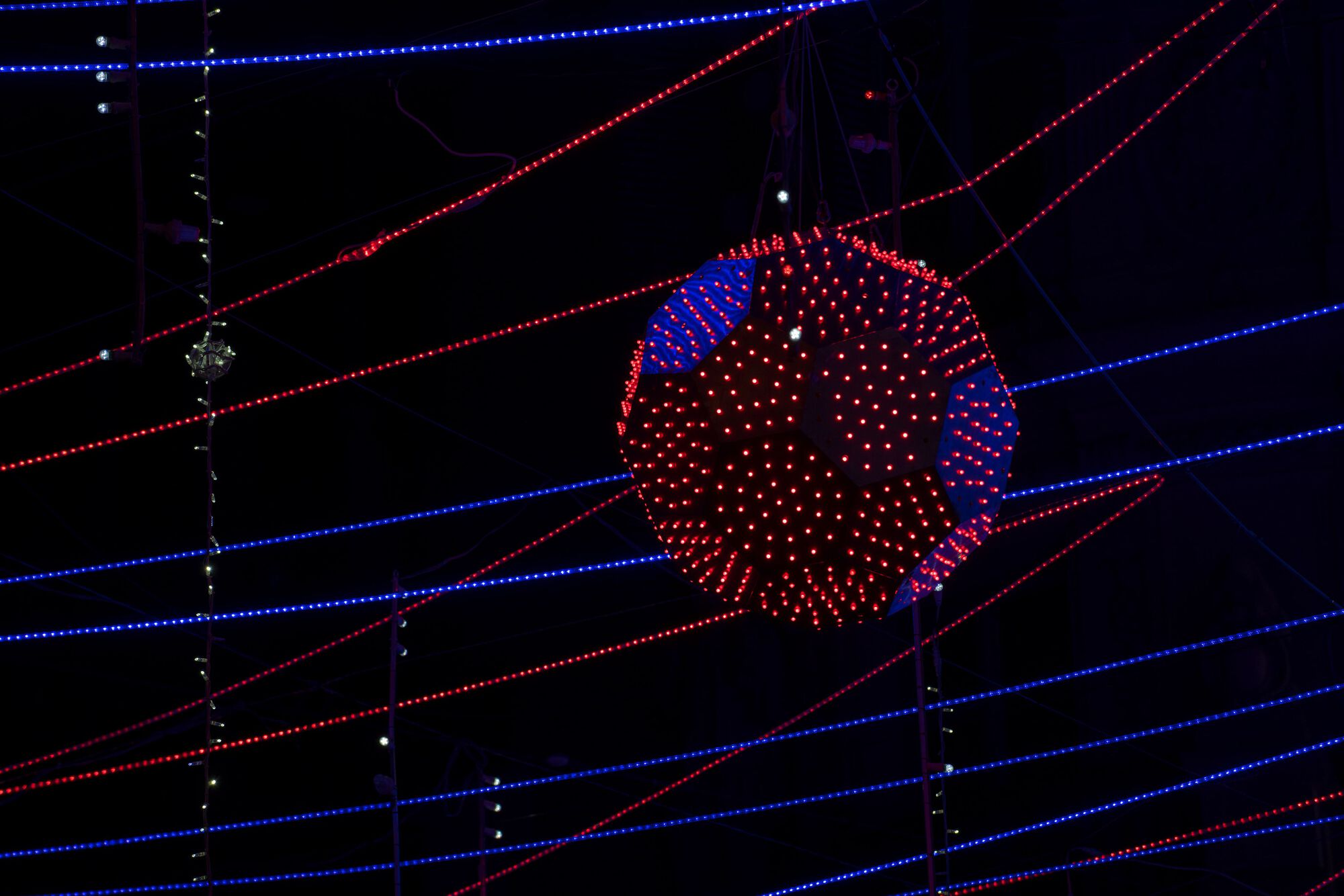 Illuminated spherical fixture with red and blue LEDs intersected by radiating horizontal light tubes at night