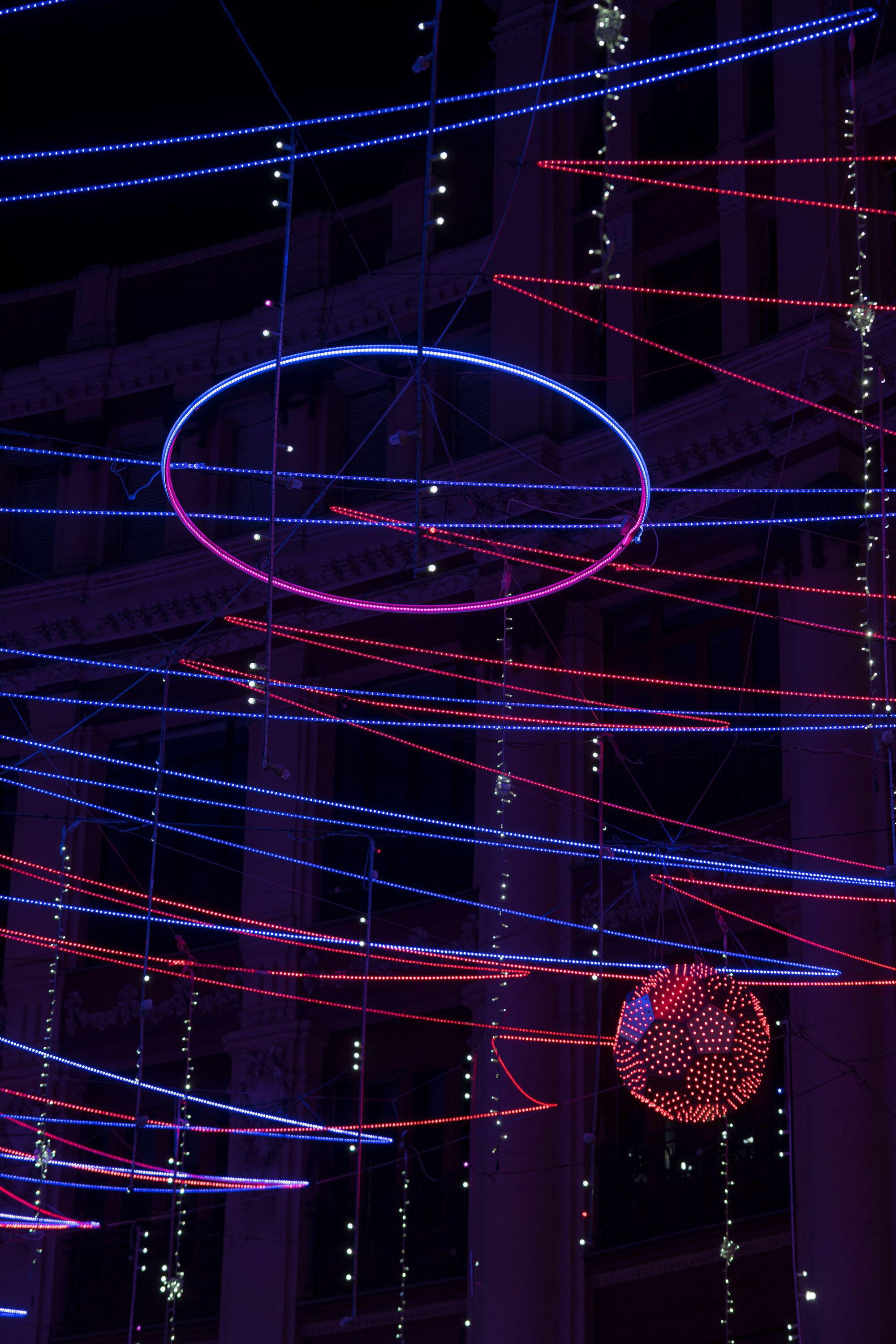 Suspended elliptical light ring with illuminated sphere hanging below among crossing diagonal LED strands