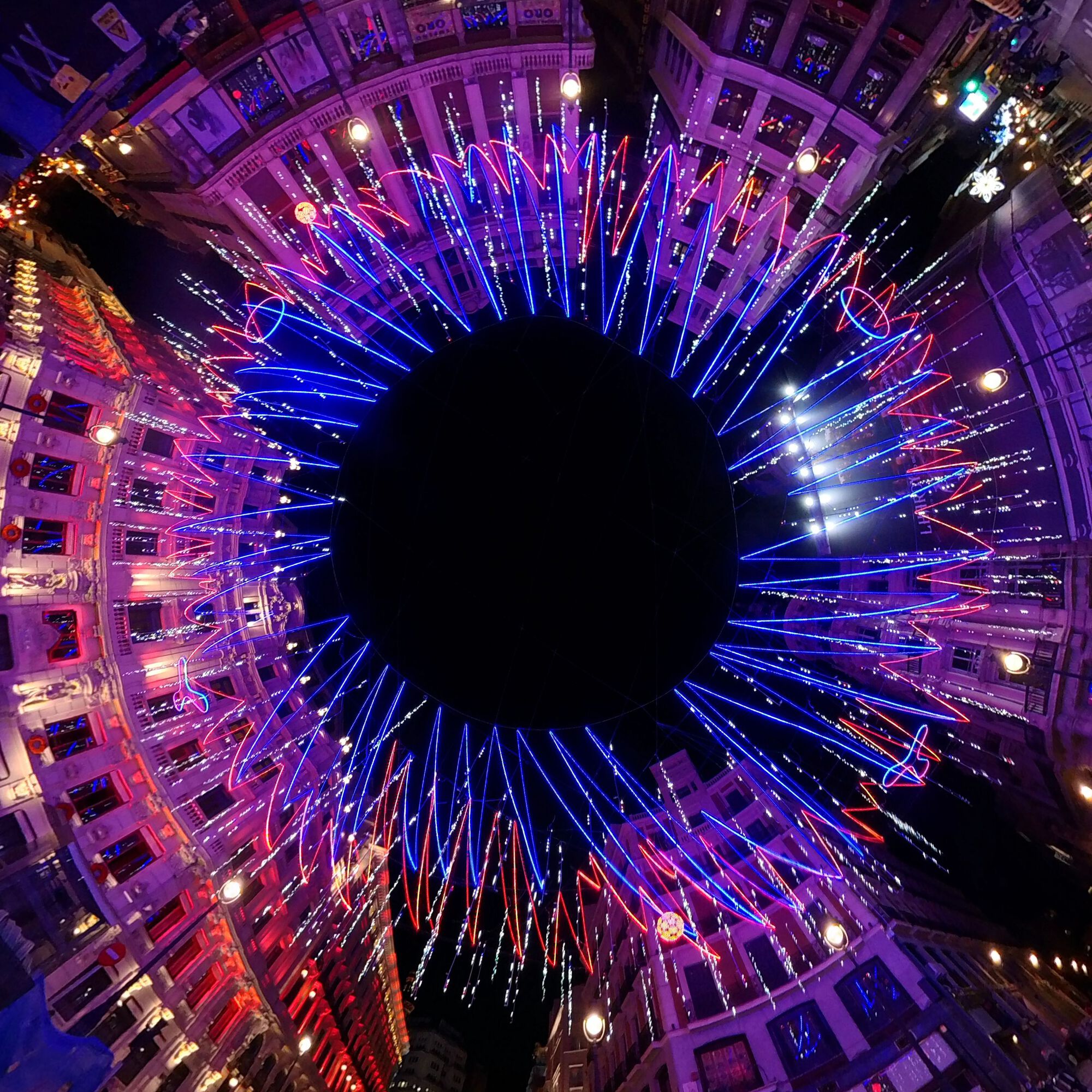 Overhead view into circular courtyard with radiating blue and red LED strands converging toward central void