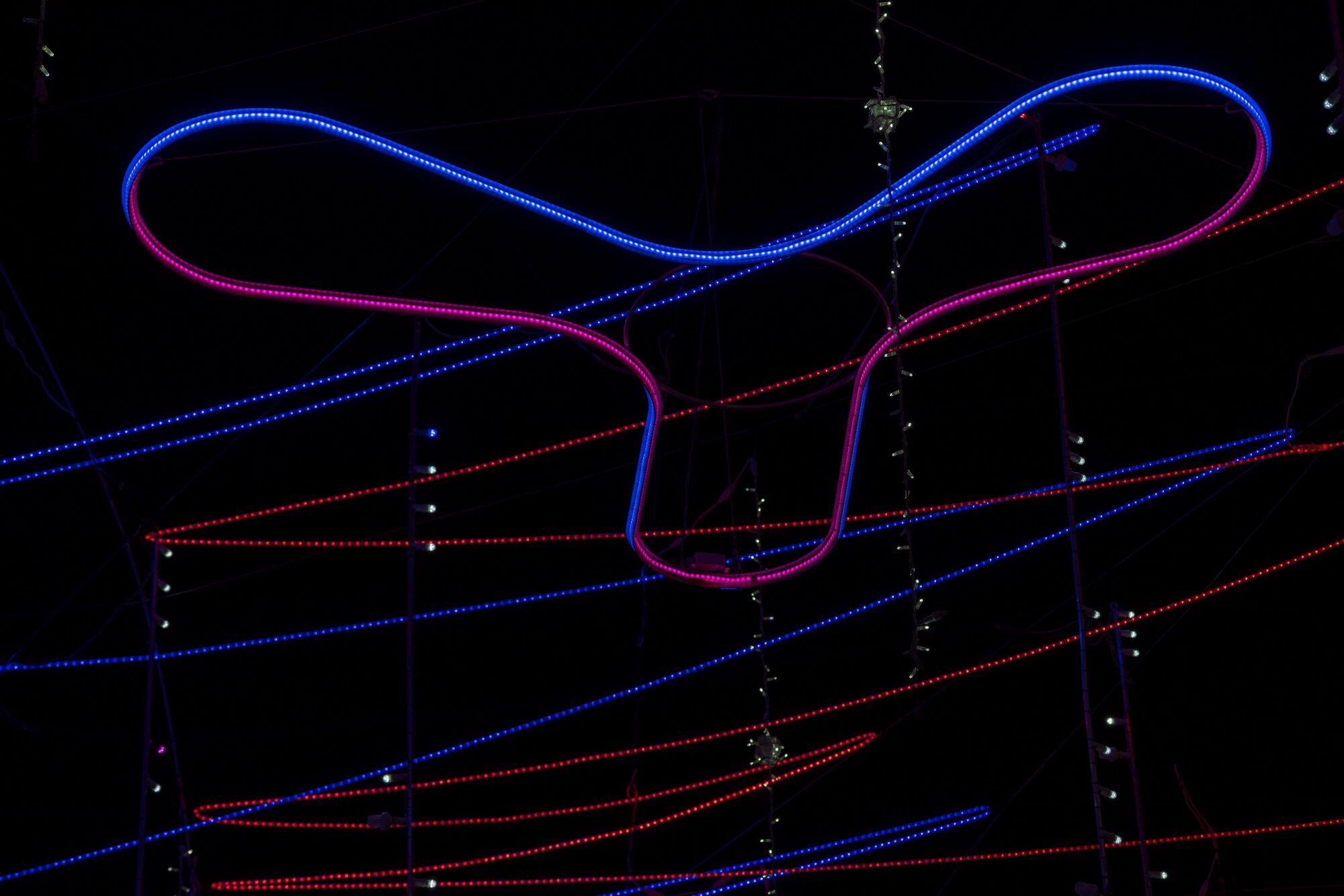 Close-up of curved LED tube forming a looping gesture against parallel red and blue linear light strands