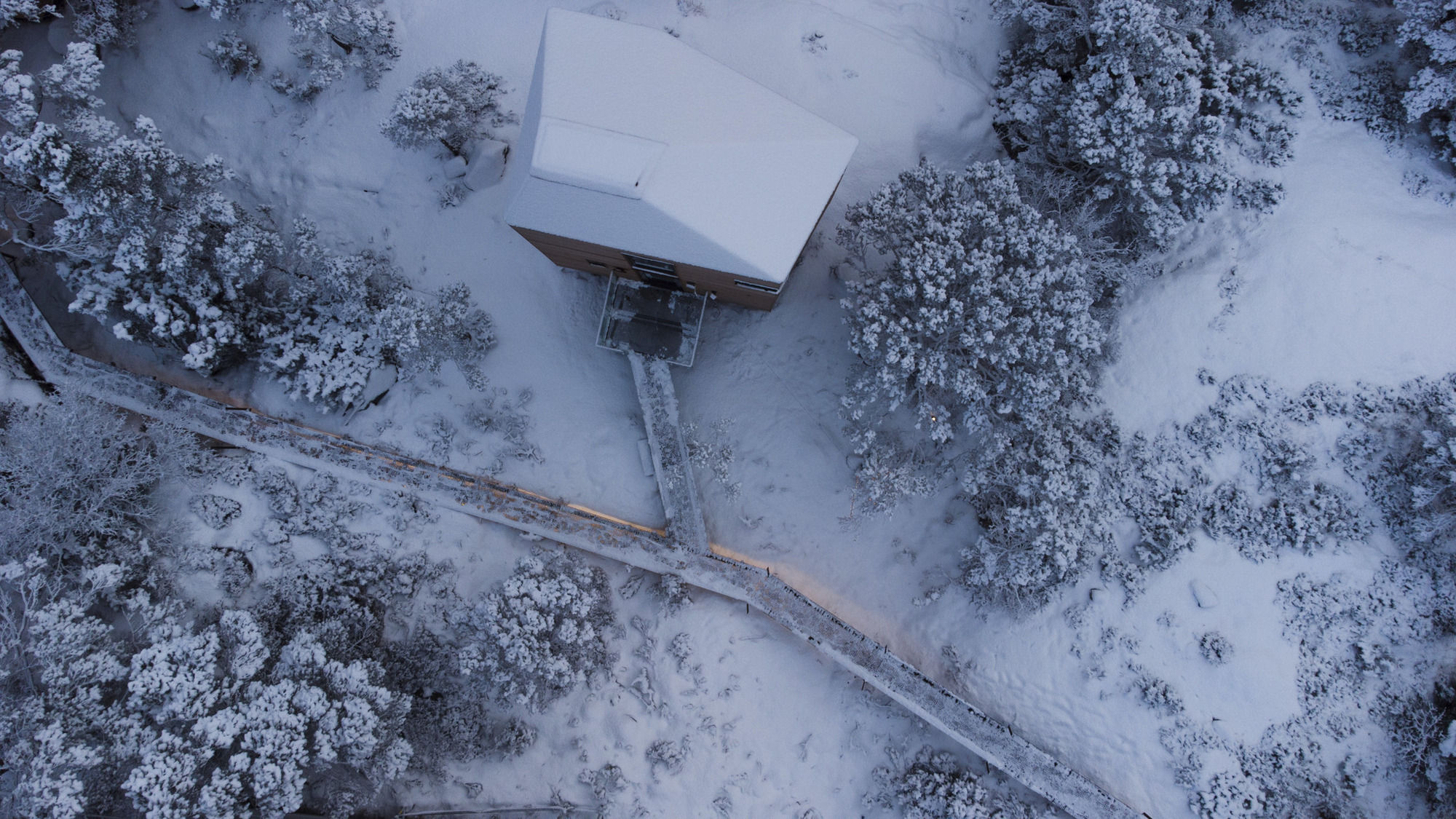 Drone view of the snow-covered volumes and timber walkway through a winter landscape
