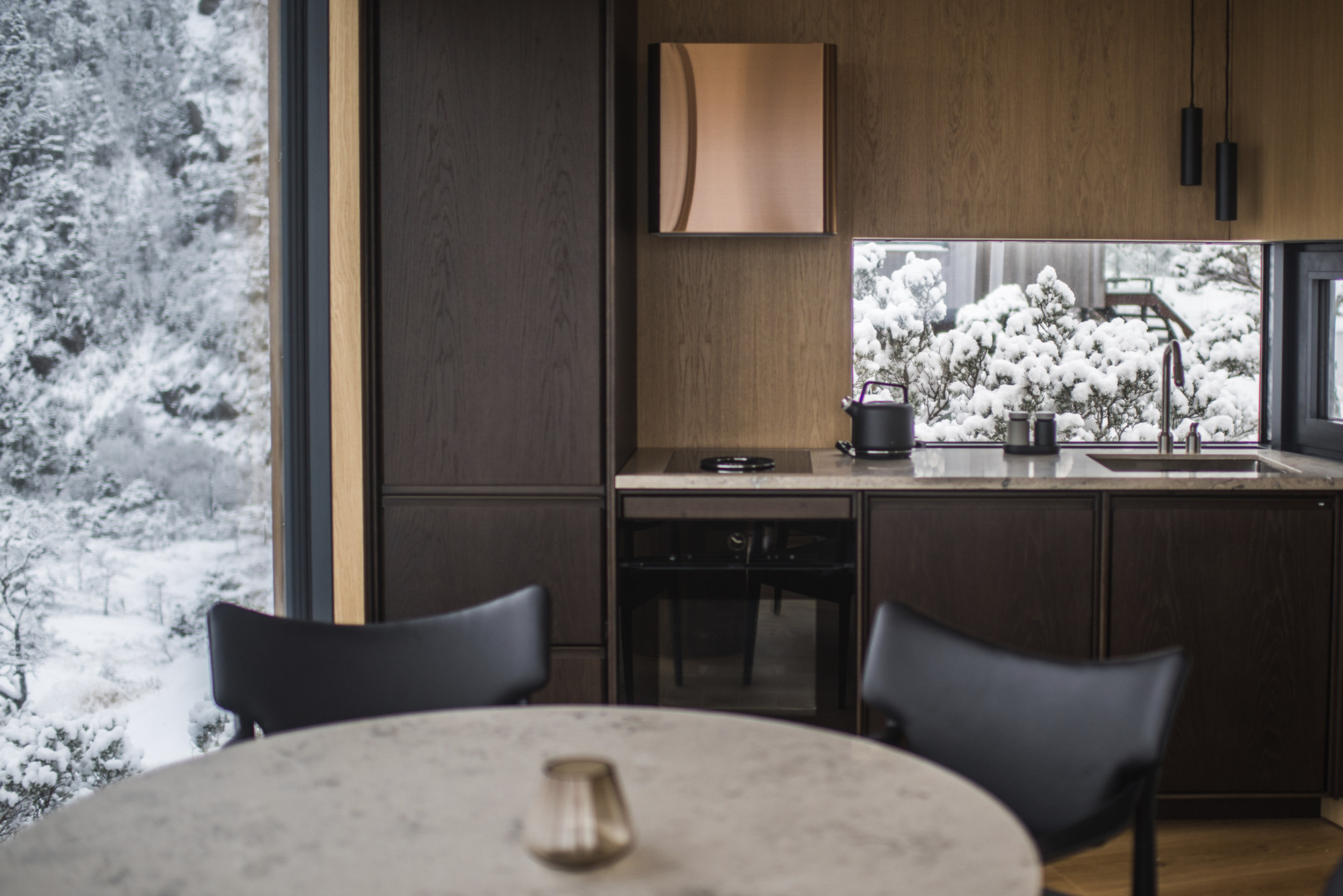 Kitchen with dark wood cabinetry and bronze fixtures framed by floor-to-ceiling windows overlooking snow-covered trees
