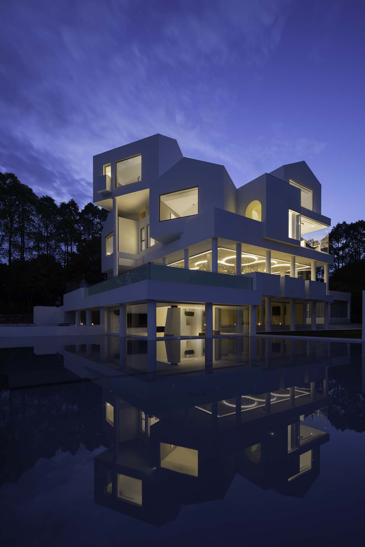 Sculptural white facade reflected in still water at twilight with glowing interior lights