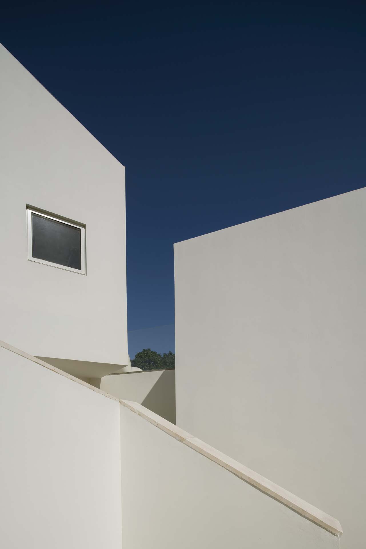 Upward view of white rendered walls meeting at an angular corner against a deep blue sky