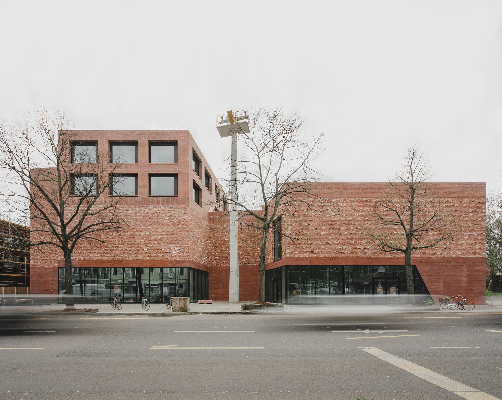 Street view of the red brick facade with arched glazed entrances and bare winter trees
