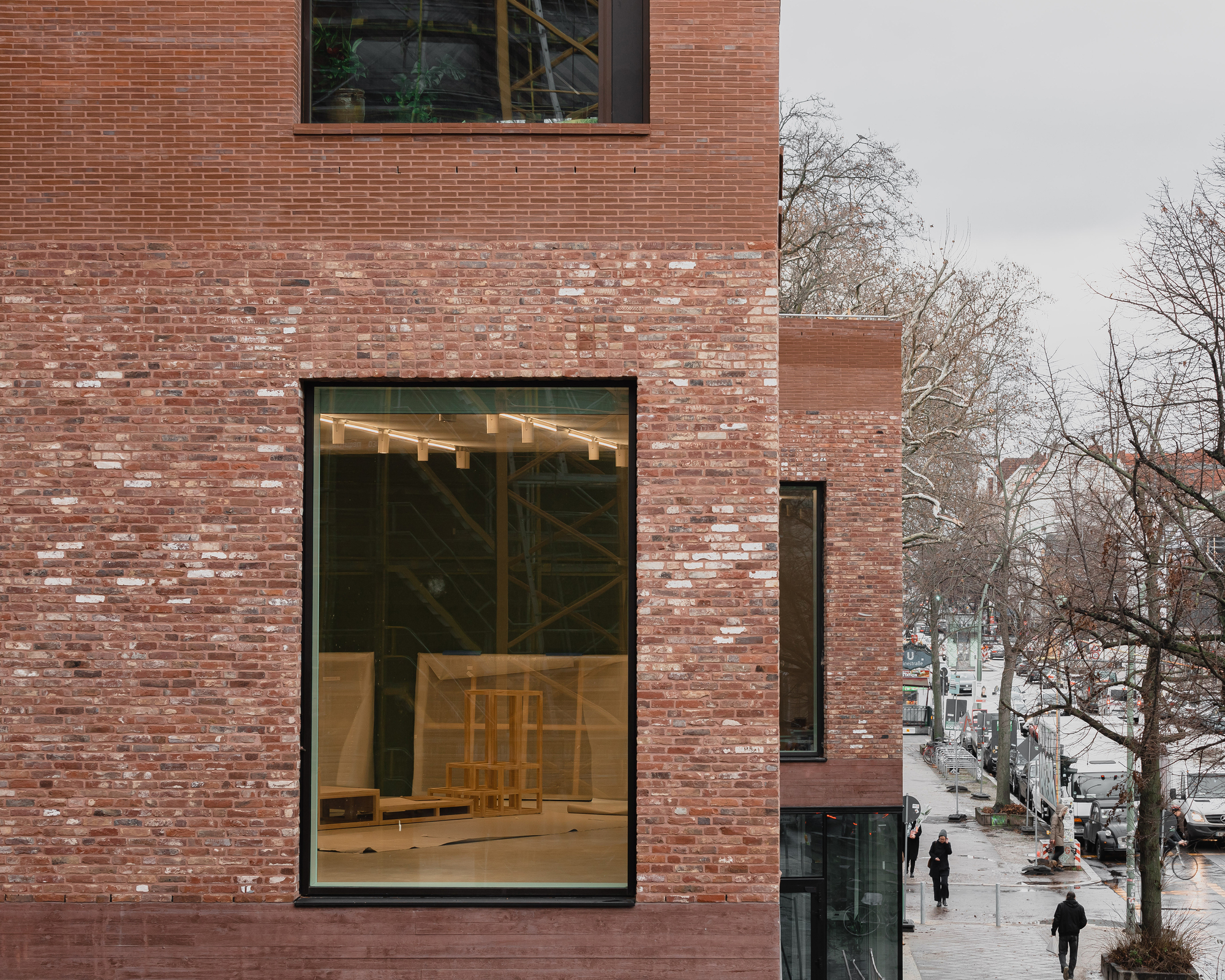 Tall glazed opening in the brick facade revealing exposed timber structure and pedestrians below