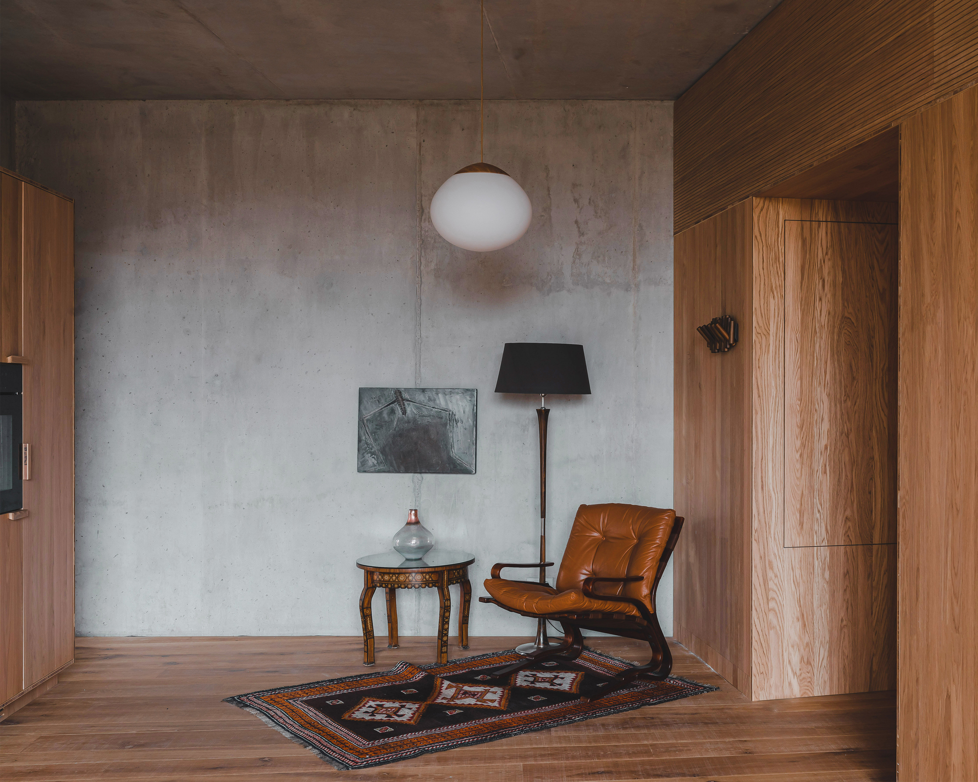 Corner reading nook with leather chair on patterned rug against concrete wall and timber paneling