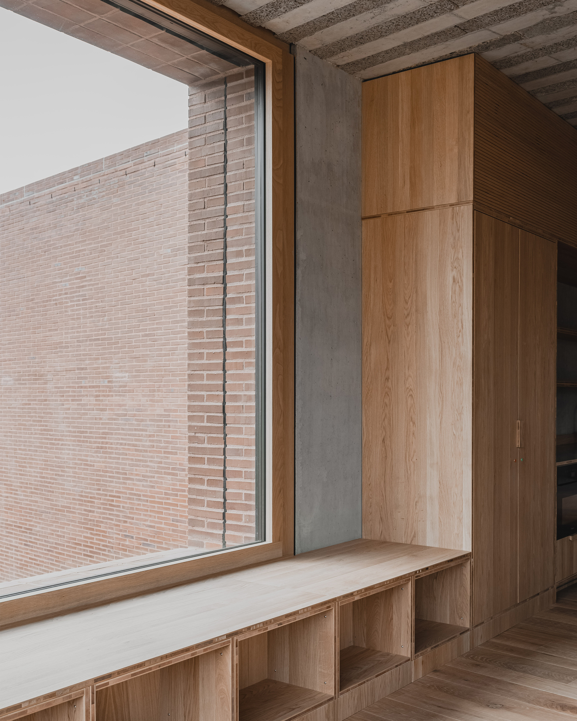 Built-in timber bench and storage units below a window overlooking a brick facade