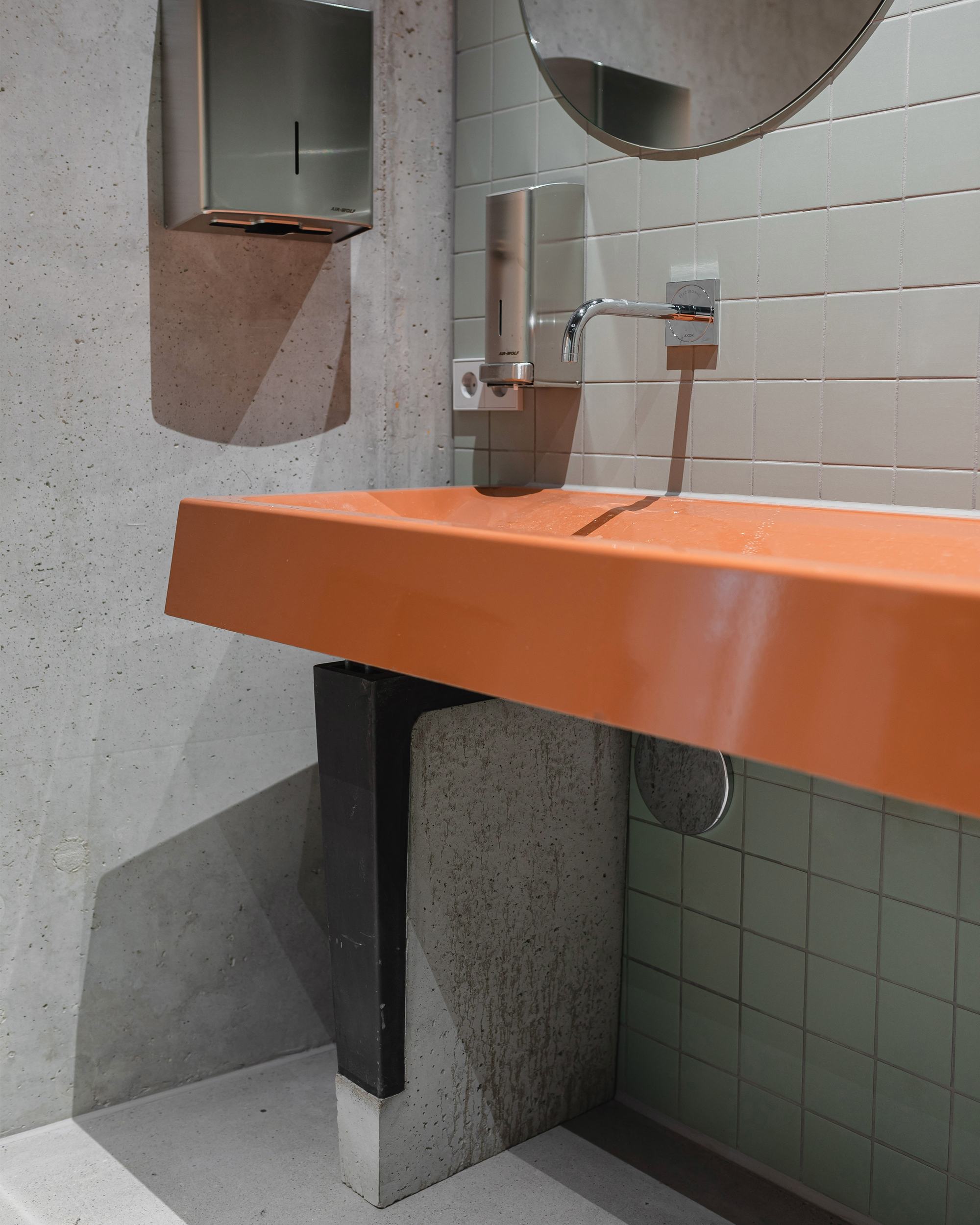 Orange concrete sink with wall-mounted faucet above white subway tiles and exposed concrete walls