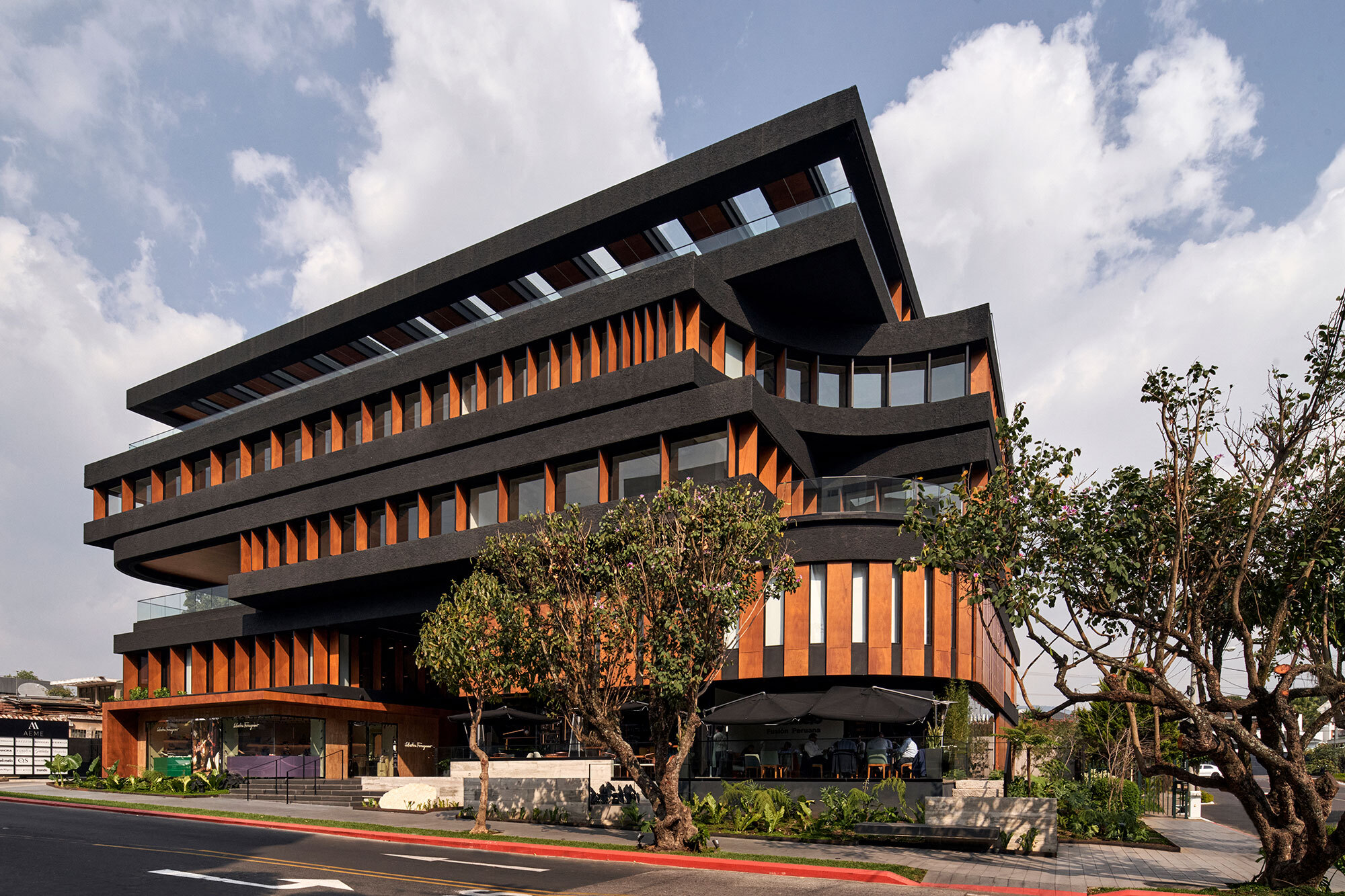 Corner view of the cantilevered floors with timber louvers and mature trees in the foreground at dusk