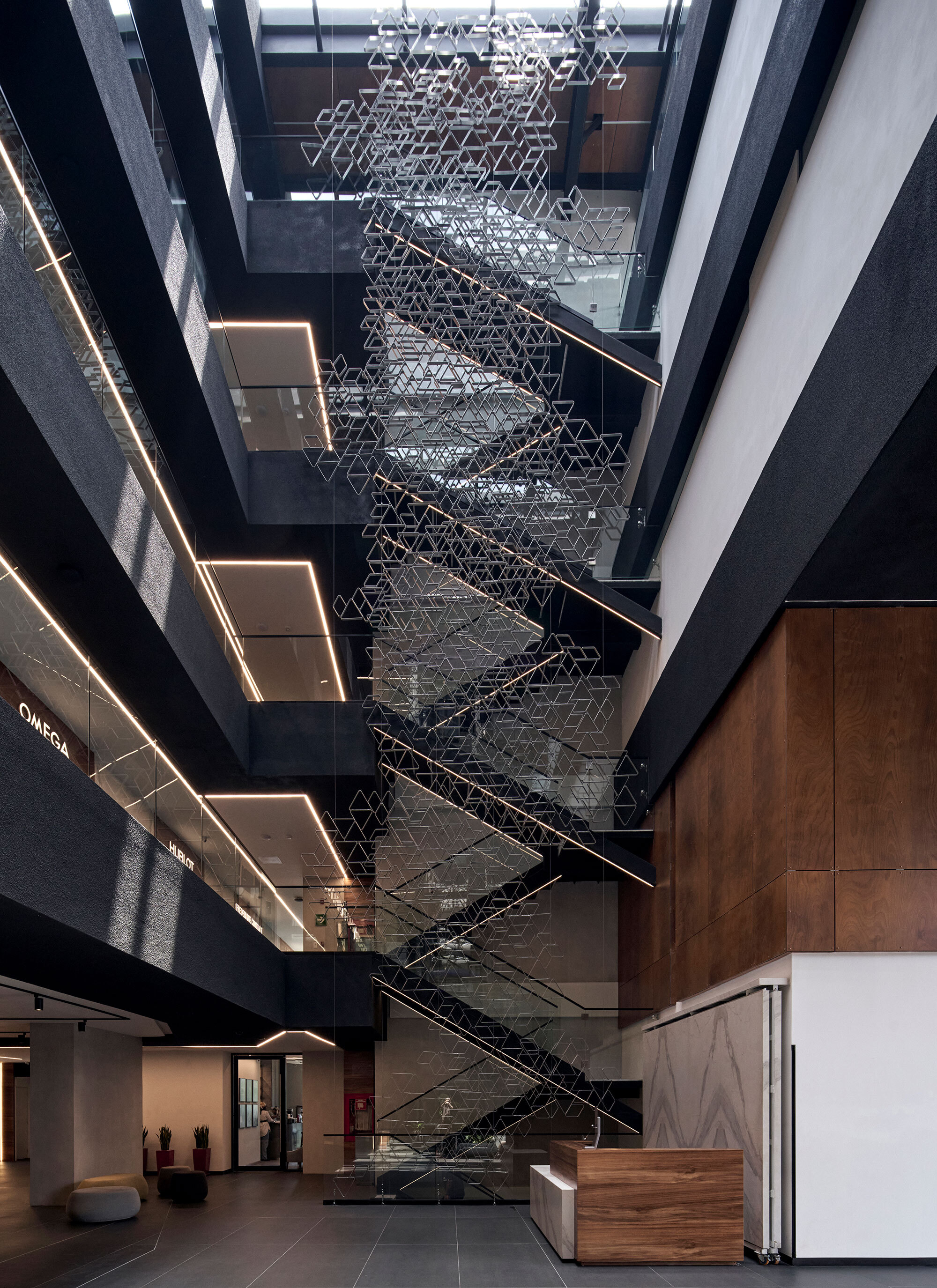 Multi-story atrium with geometric metal sculpture suspended above the central staircase and timber reception desk