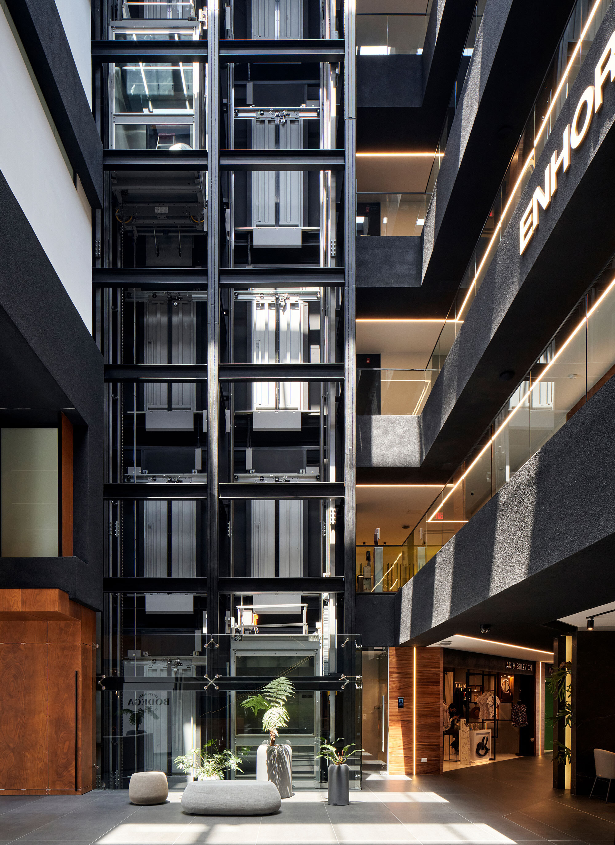 Interior atrium with exposed glazed elevators and planted planters on a white tile floor
