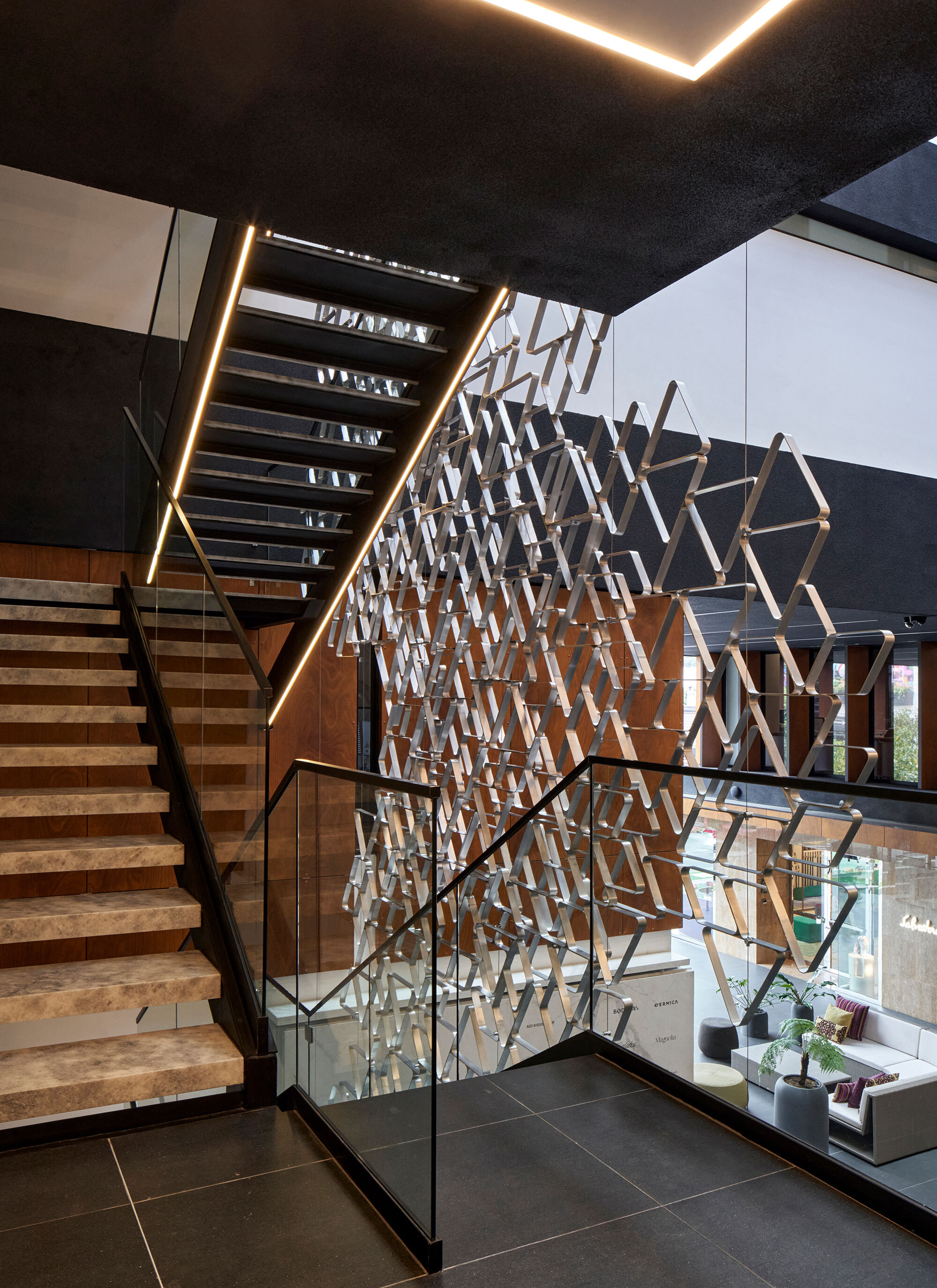 Timber staircase alongside the perforated metal screen with glass balustrade and recessed ceiling lighting