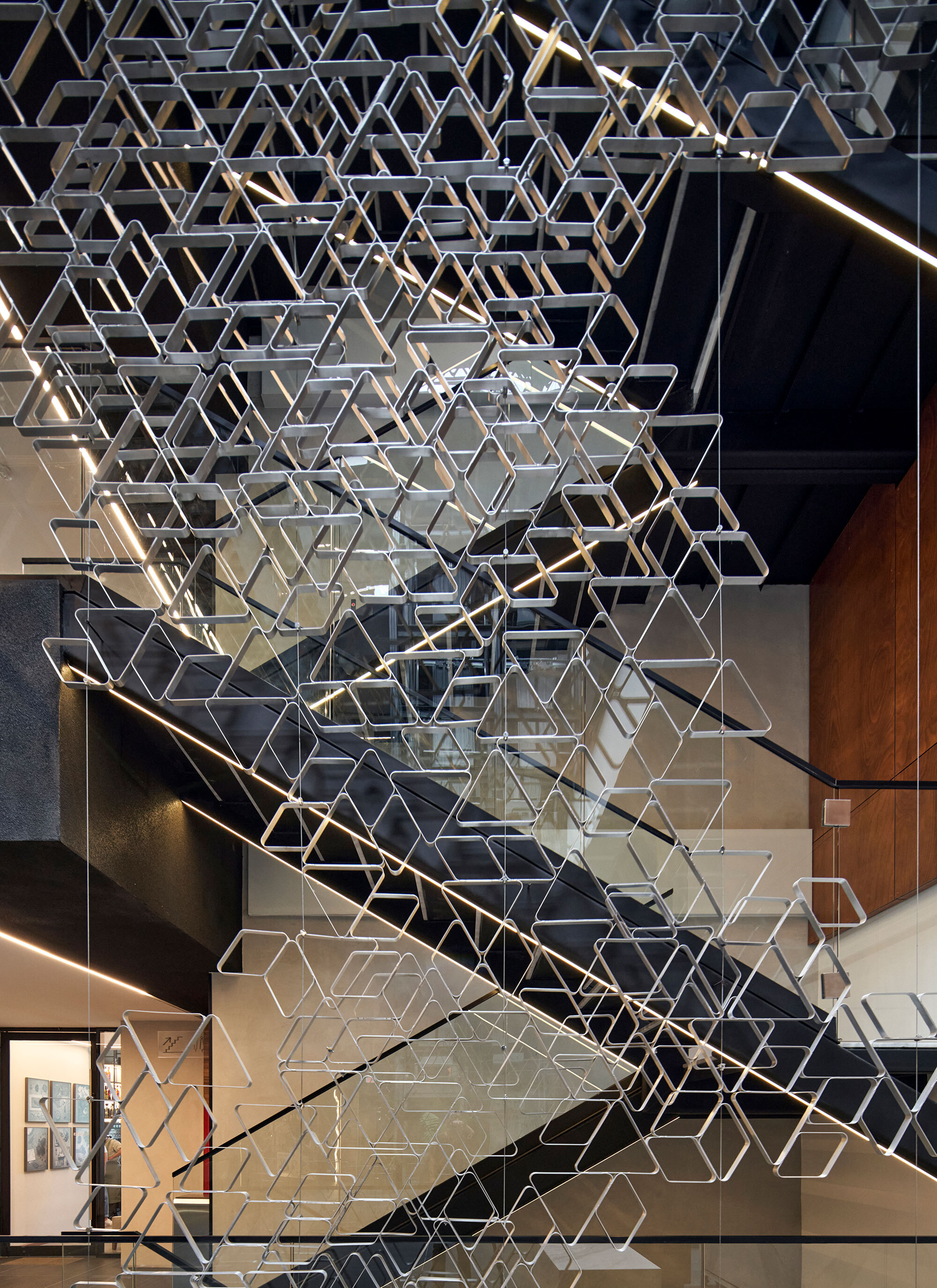 Suspended hexagonal metal screen hanging above a staircase with linear lighting on the treads