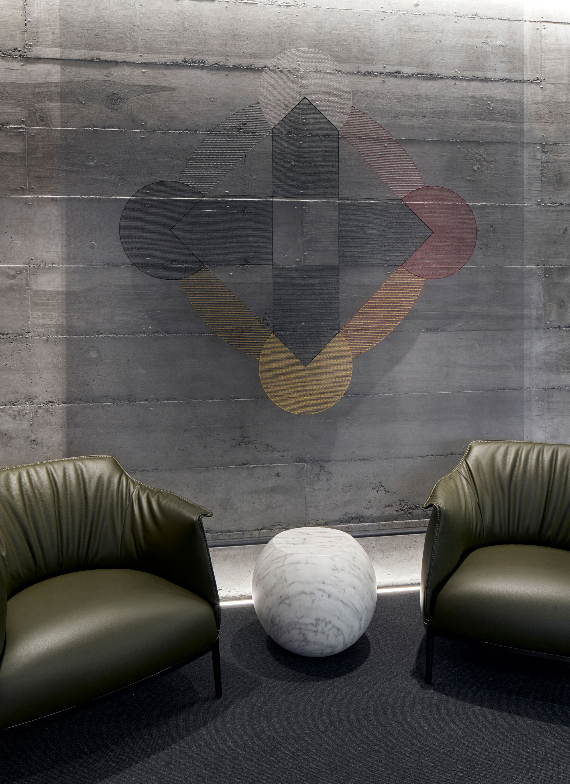 Concrete wall with geometric artwork above two green leather chairs and a marble side table