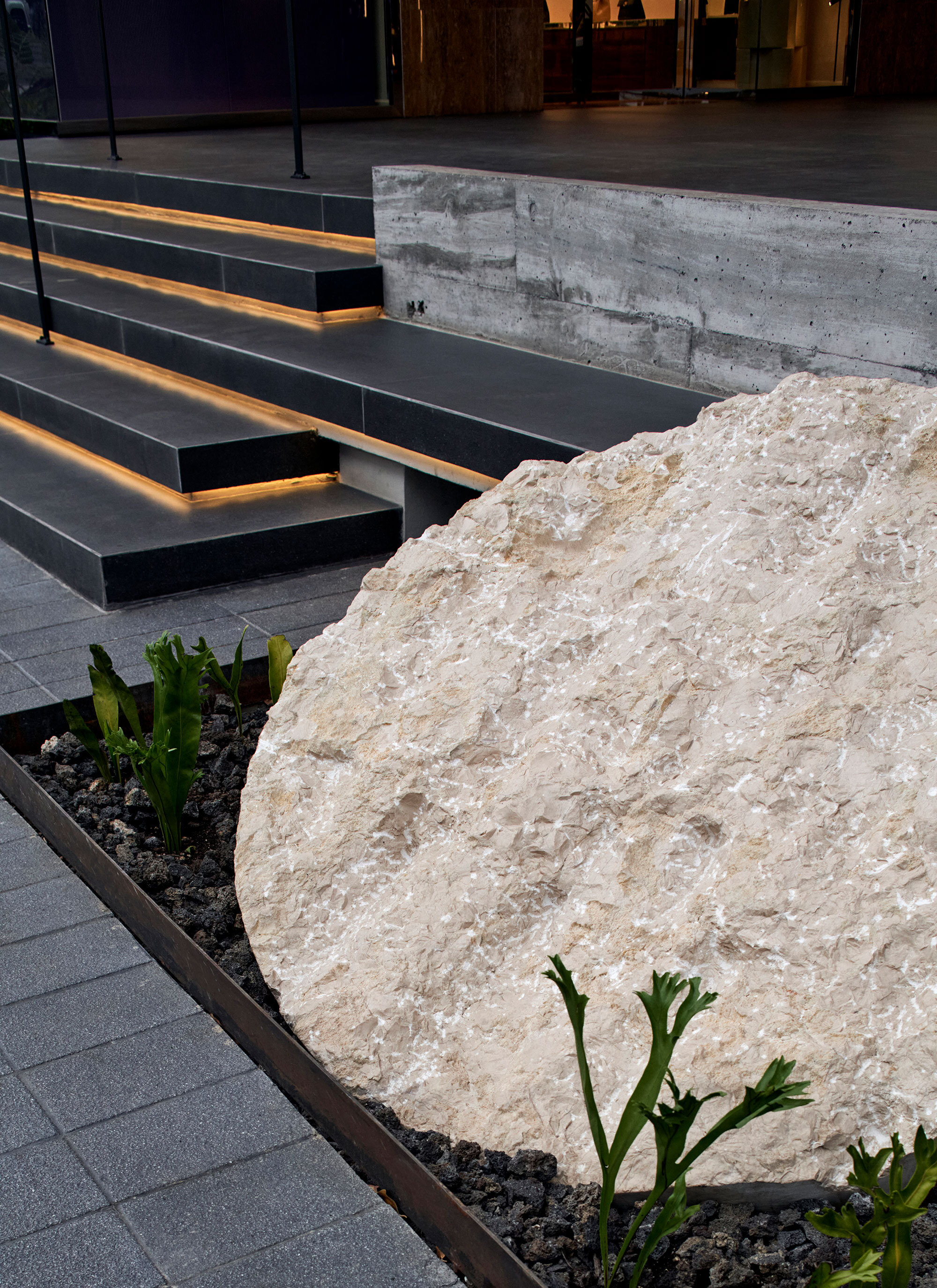 Textured limestone boulder beside planted bed with black steel stairs and integrated strip lighting