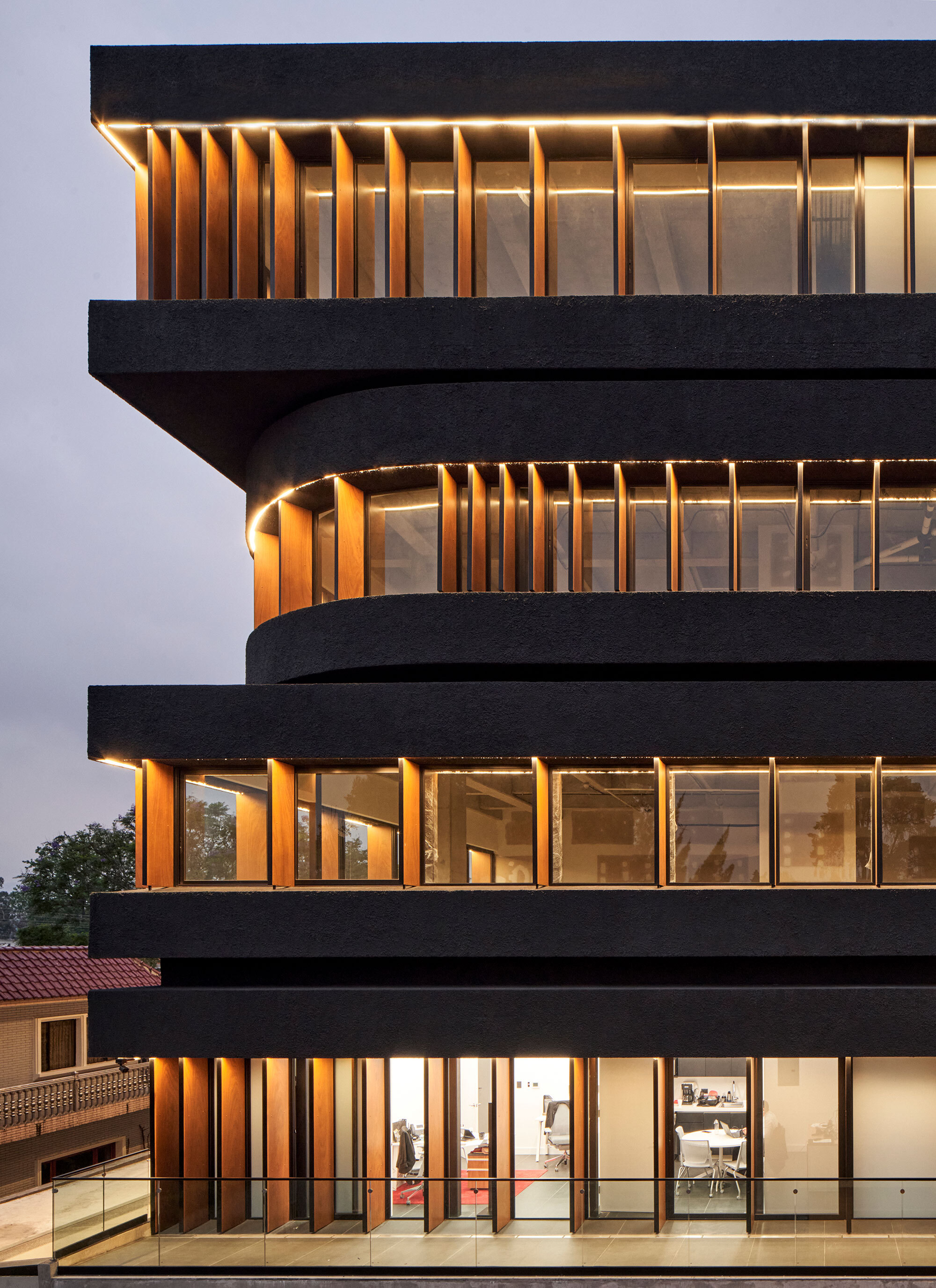 Detail of the cantilevered floor slabs with vertical timber fins between dark horizontal bands at dusk