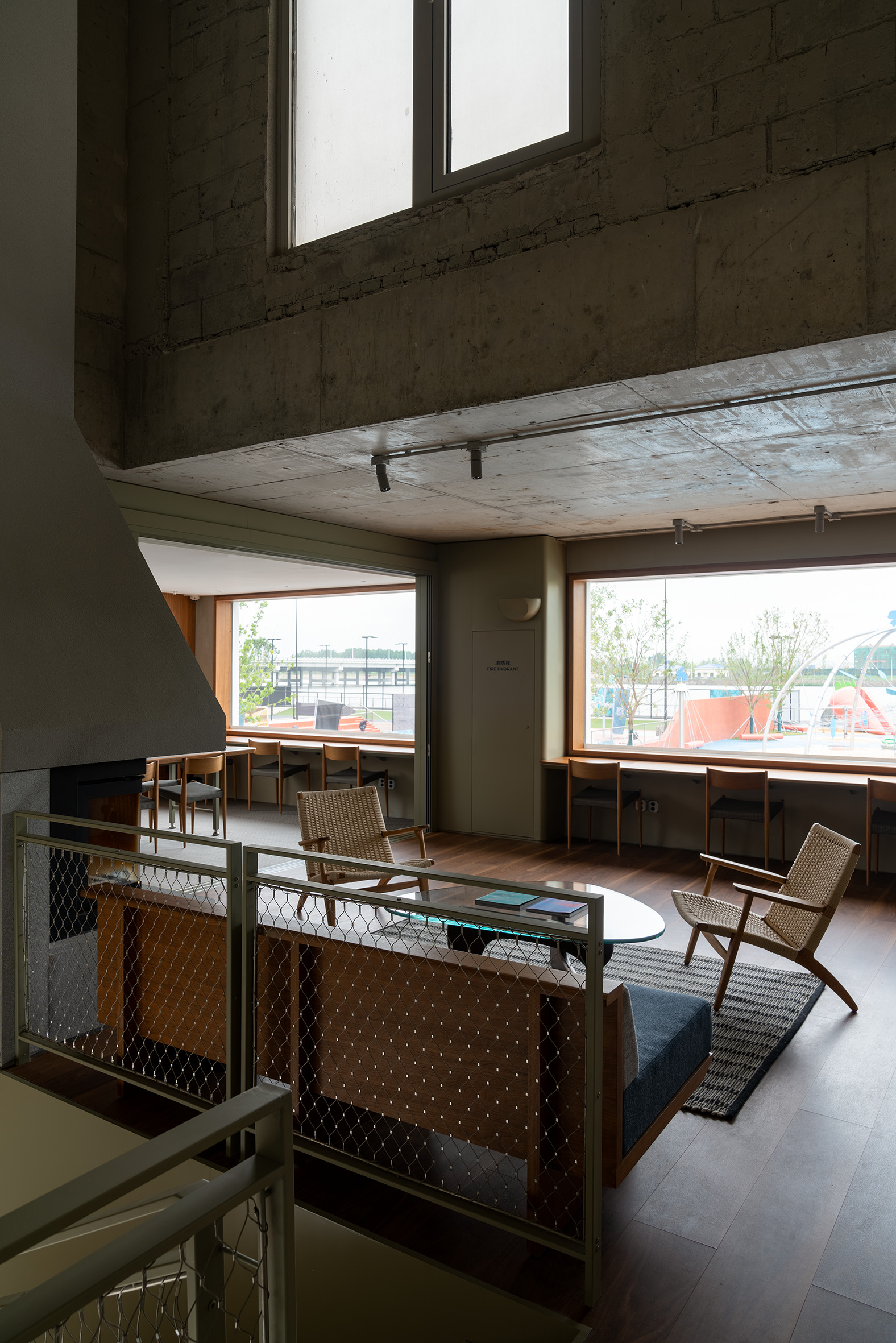 Mezzanine lounge with woven chairs and angled windows framing views of outdoor terrace and trees