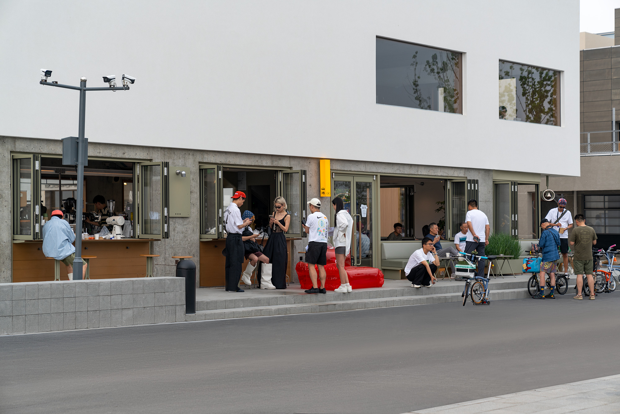 Folding storefront windows opening onto plaza where crowds gather on a sunny afternoon