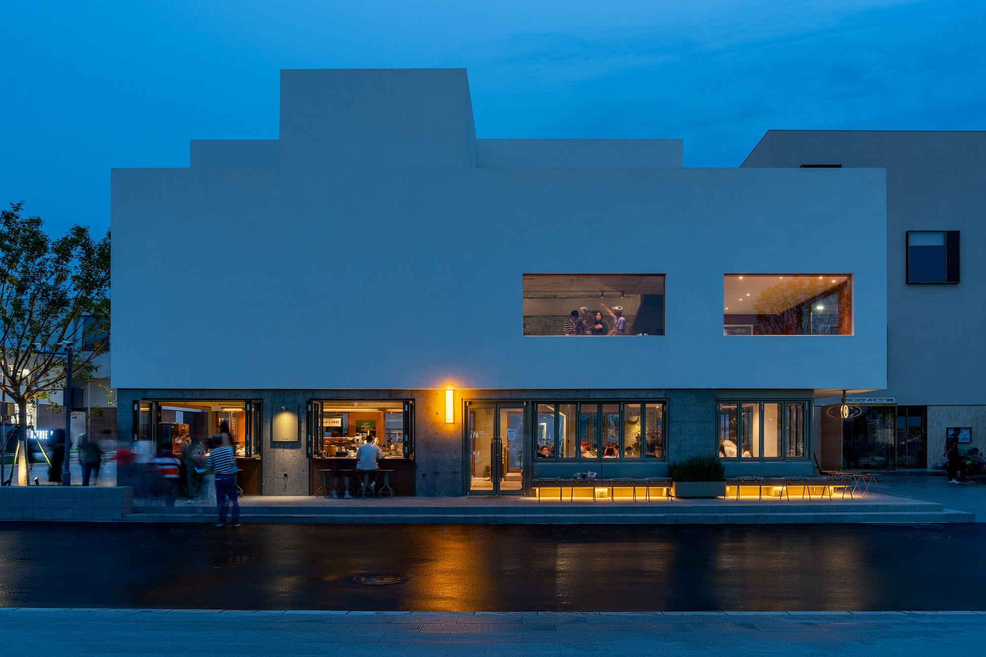 White stepped facade with horizontal window openings and warm interior lighting at twilight