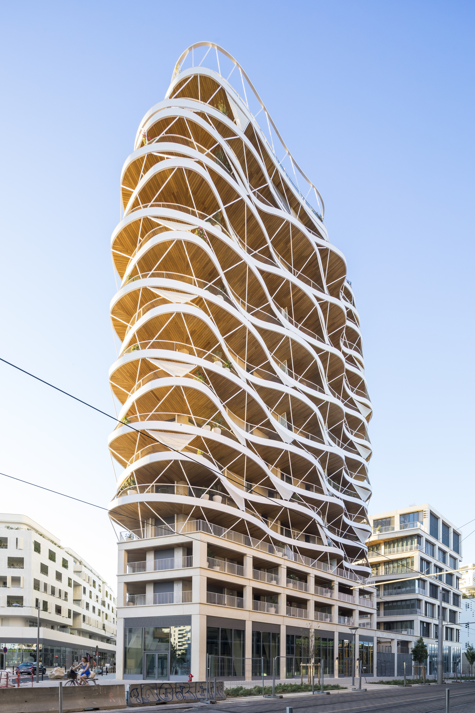 The helical tower facade with white diagonal bracing and timber-clad balconies seen from street level