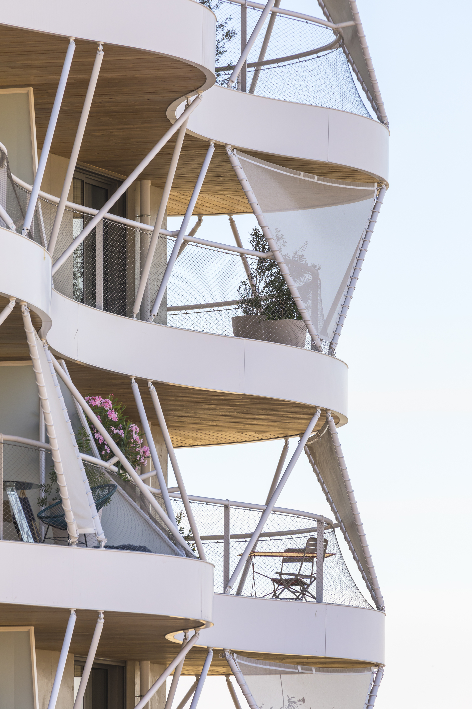 Close-up of stacked balconies with timber soffits, white diagonal struts, and mesh safety screens