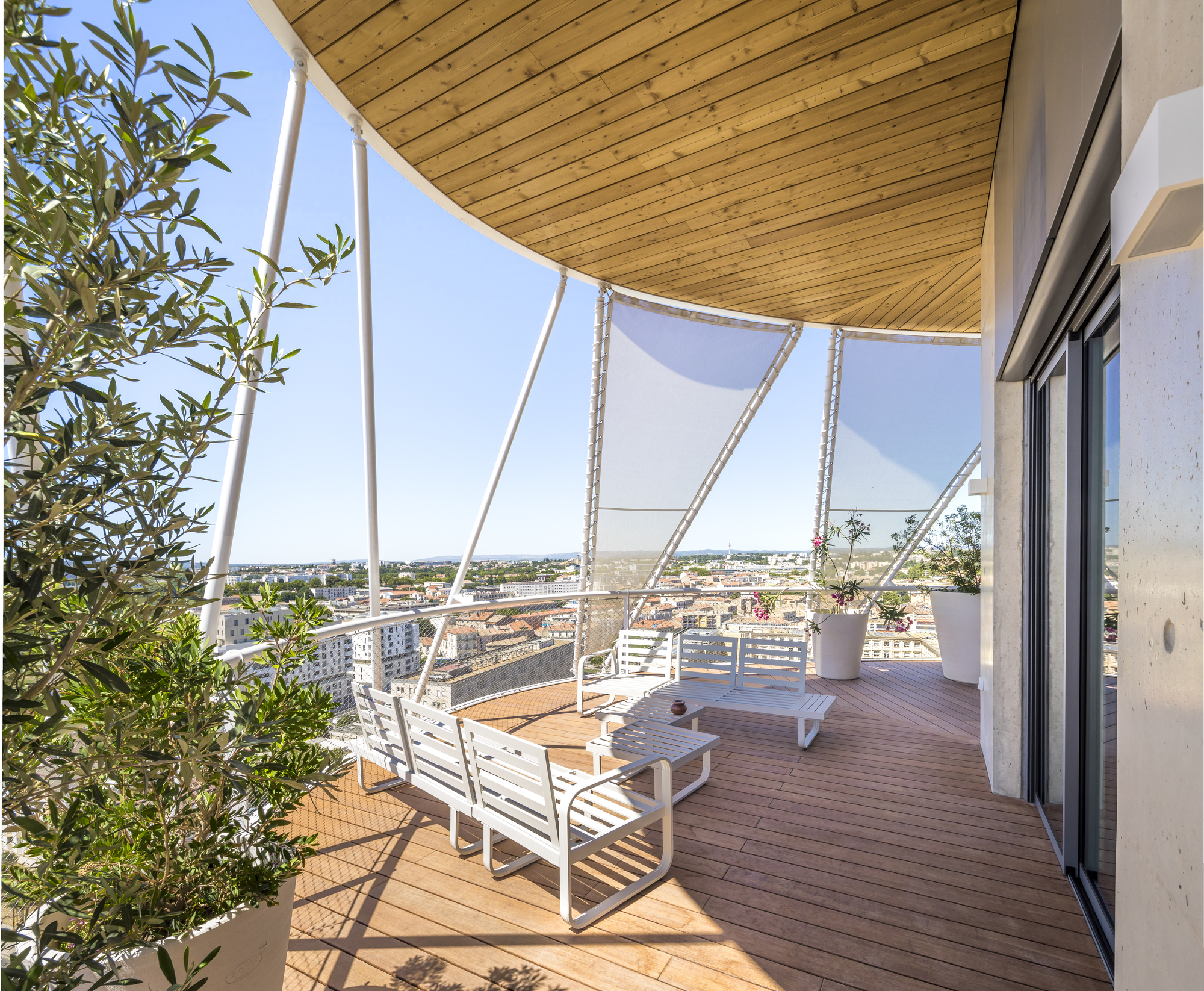 Terrace with timber decking and curved wood ceiling under white structural arms and mesh screens